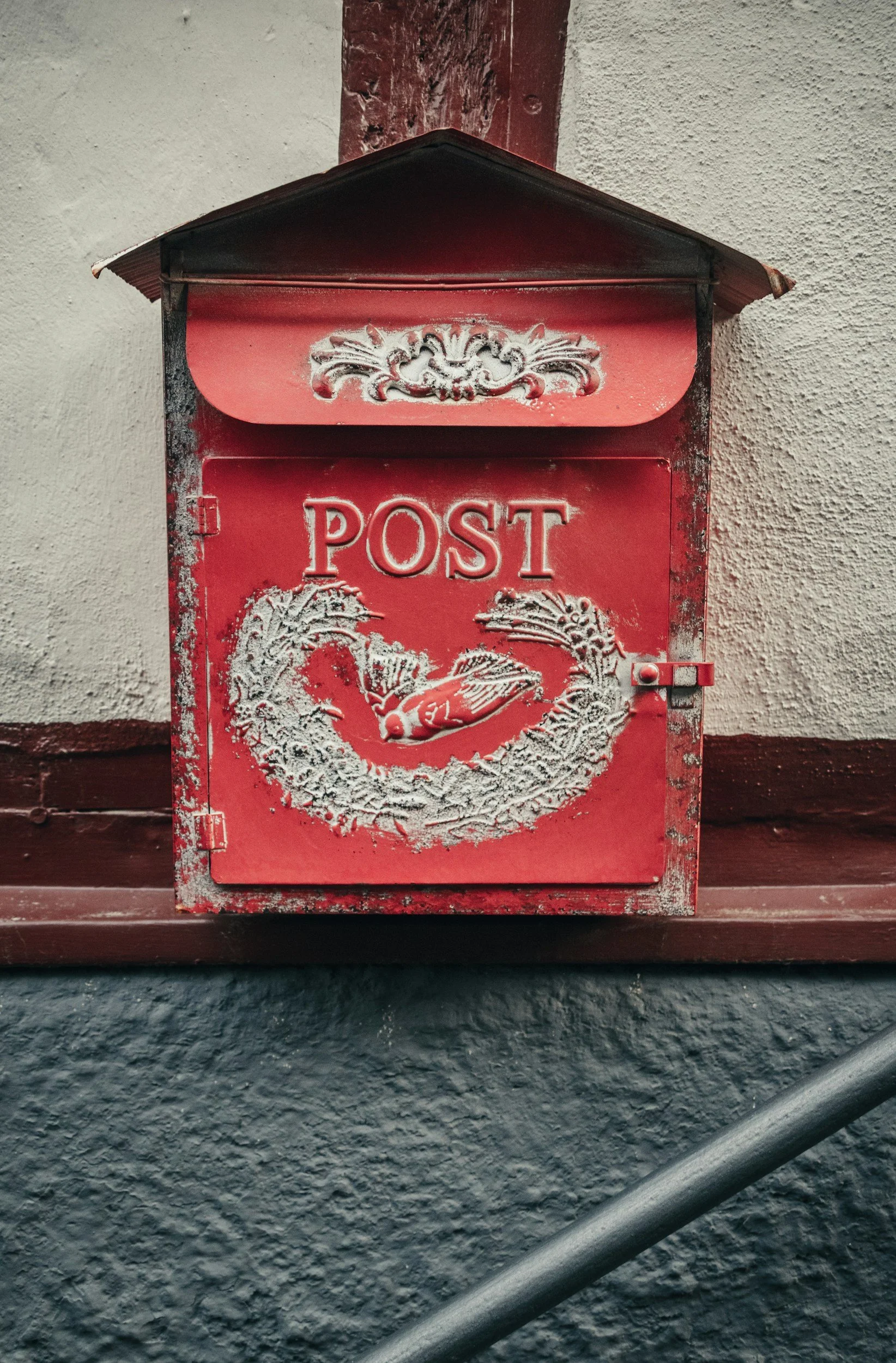 A decorative white mailbox with ornate details and the word "POST" on it, mounted on a stone wall.