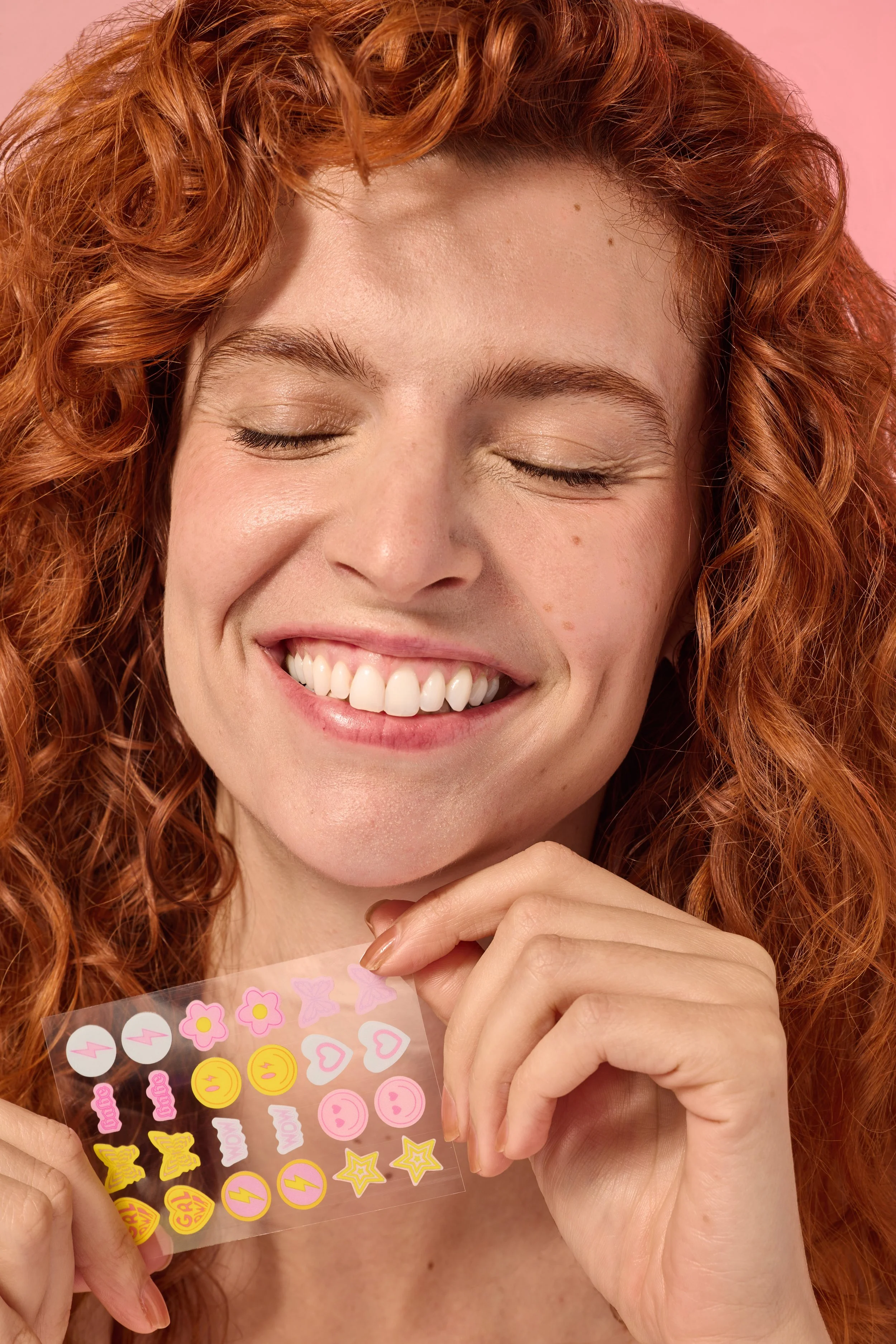 Woman with red hair smiling while holding colorful beauty acne stickers, beauty product photography by Golden Joy Photography in Los Angeles