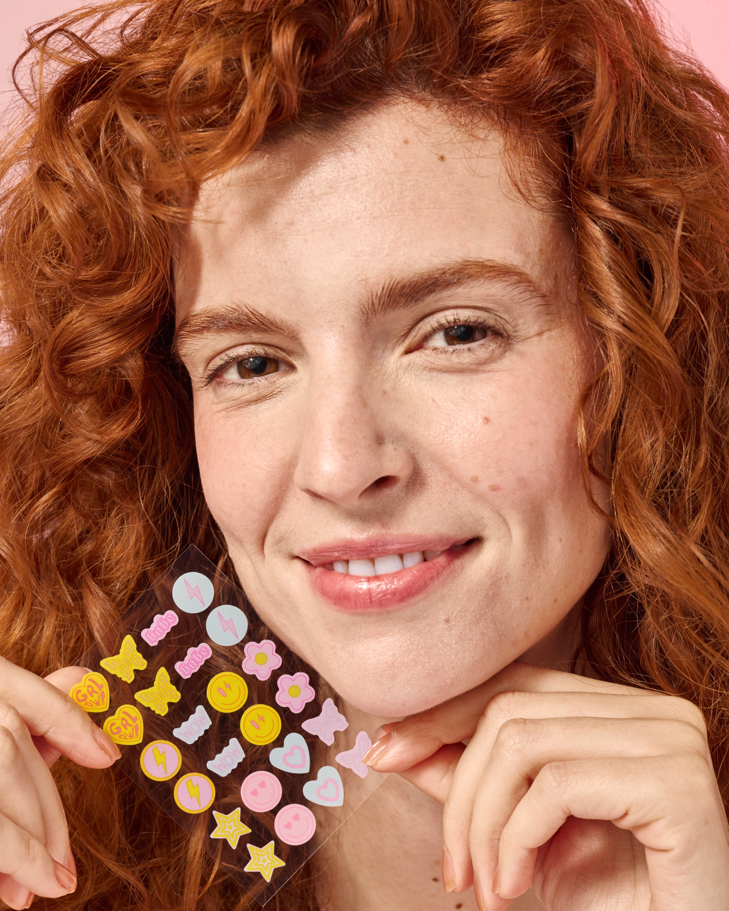 Woman with red hair holding colorful beauty acne clearing stickers near face, beauty product photography by Golden Joy Photography in Los Angeles