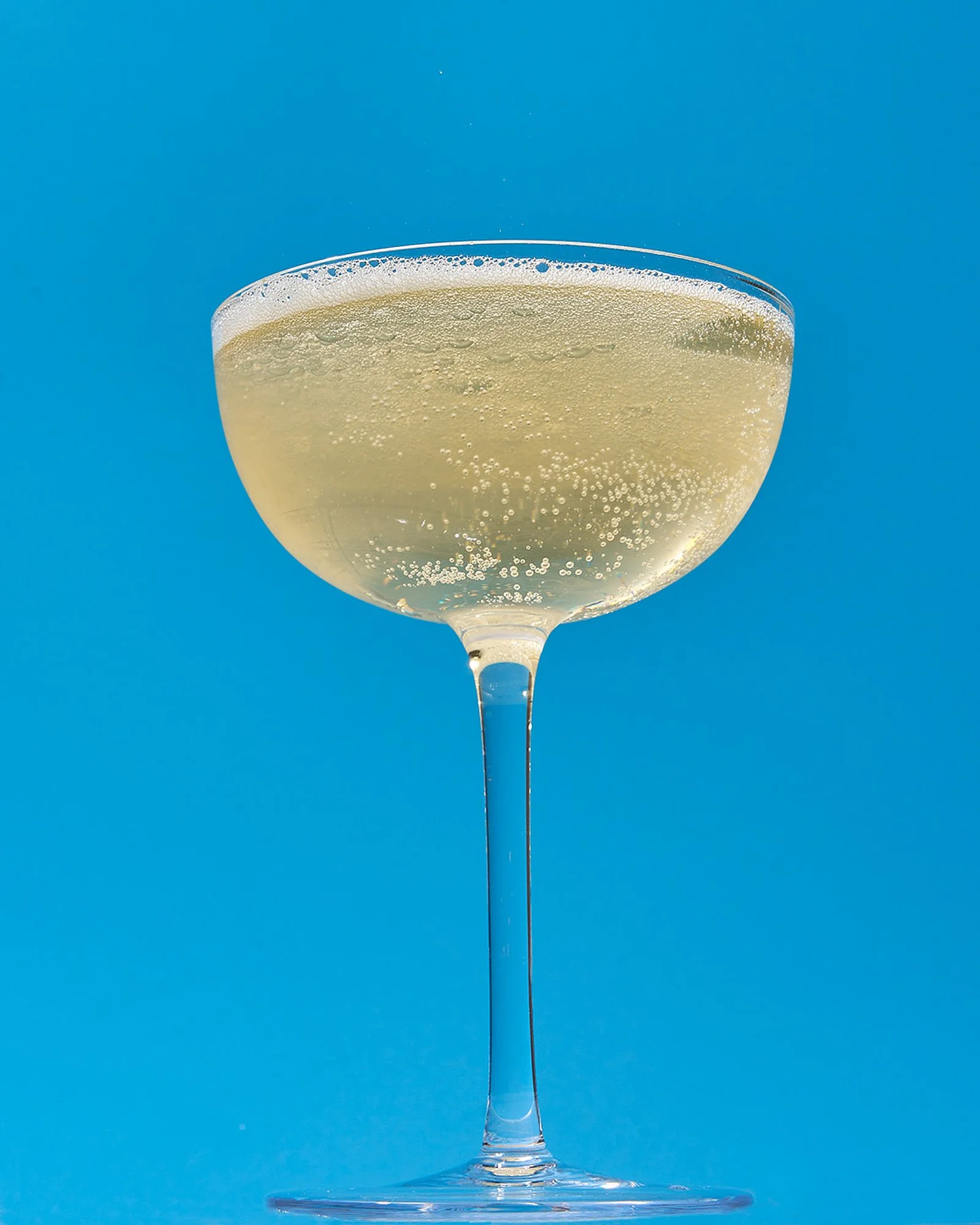 Champagne coupe with sugar rim on bright blue background, product beverage photography by Golden Joy Photography in Los Angeles