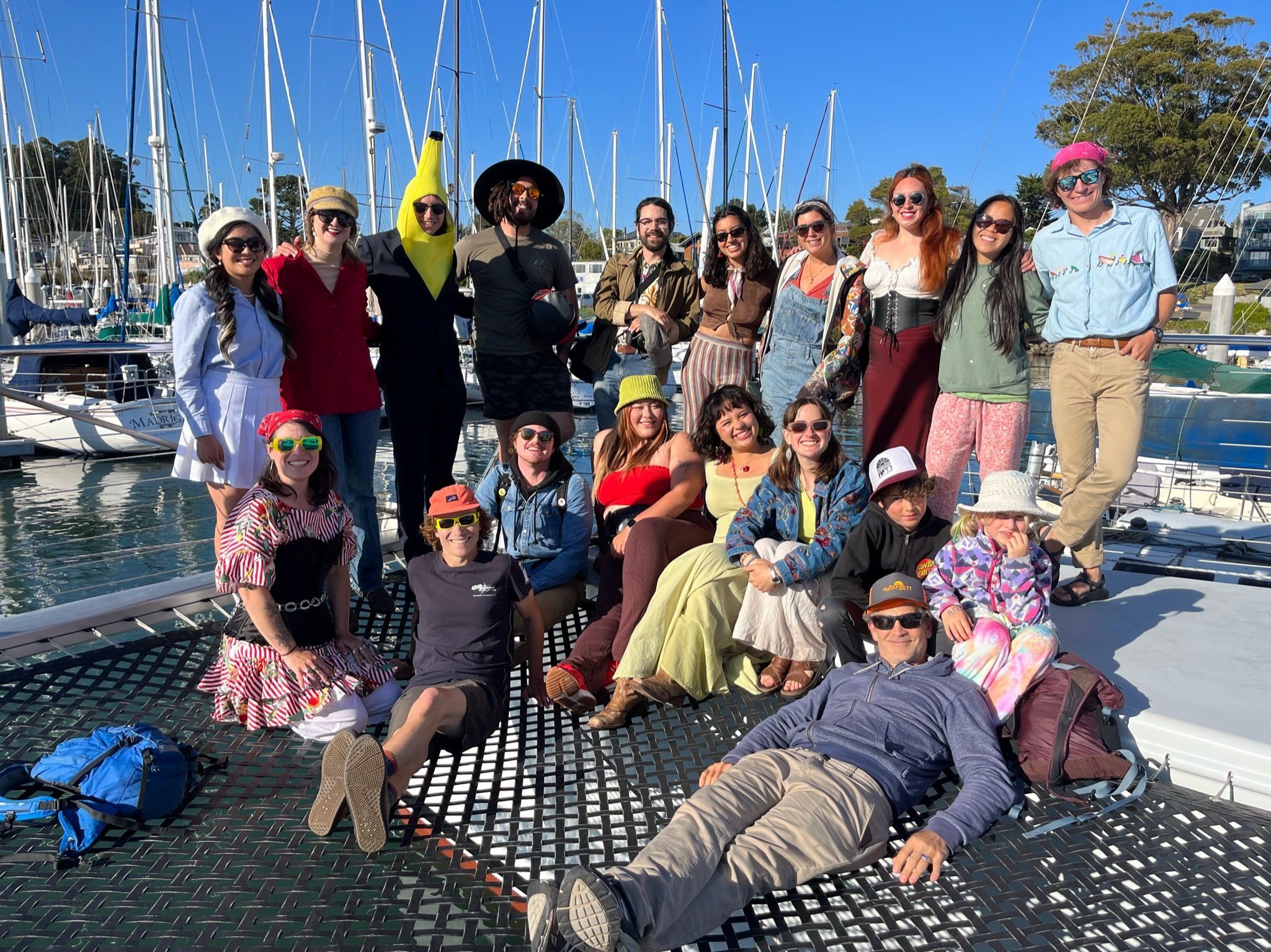 A team of coworkers gathers at the front of the boat on the net for a group photo, everyone is happy and festive wearing costumes for their fun team building private event