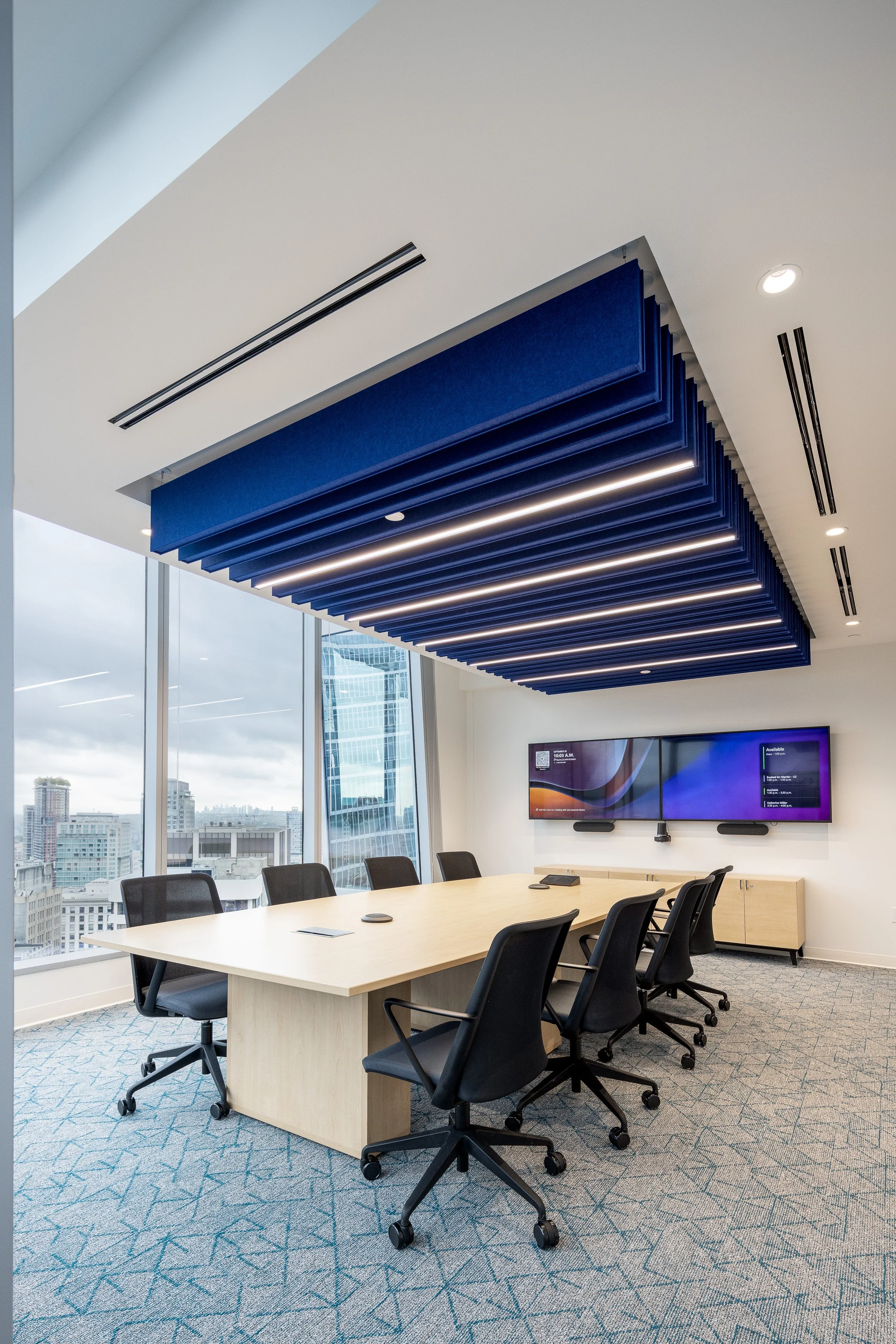 Modern conference room at the Mott MacDonald Vancouver office with a large meeting table, task chairs, acoustic ceiling baffles, and floor-to-ceiling windows.