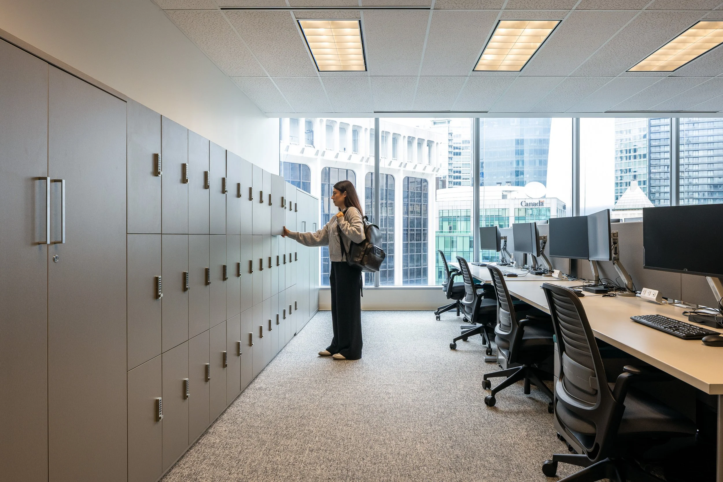 Employee accessing integrated storage lockers beside open workstations at the Mott MacDonald Vancouver office.