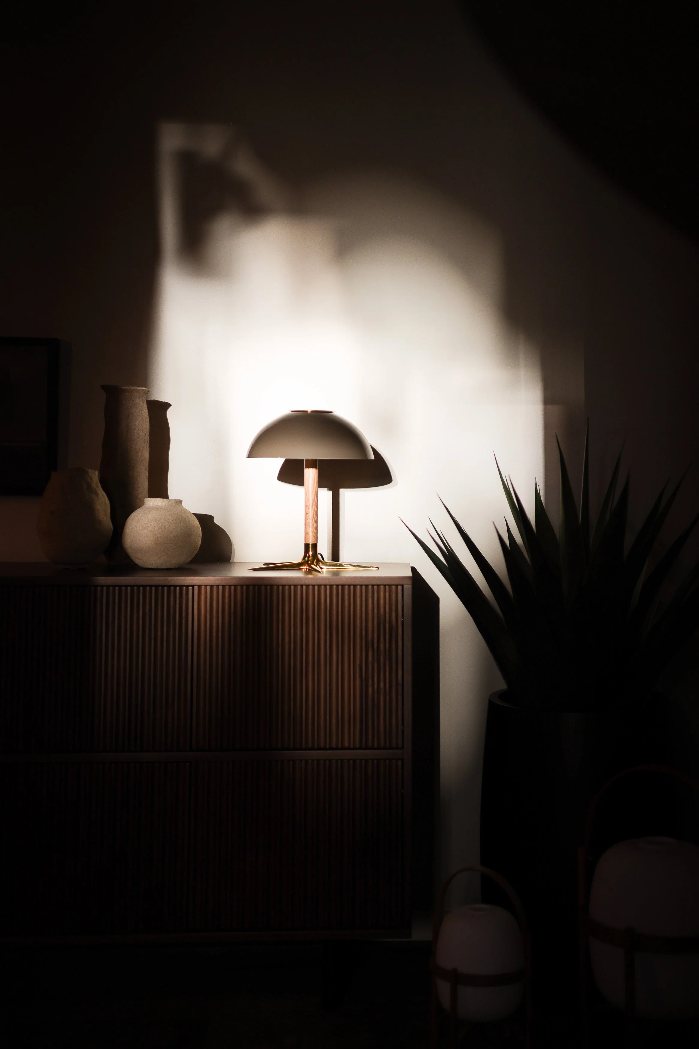 Ribbed wood sideboard vignette with ceramic vessels, a dome table lamp, and dramatic shadow play in the Lightform showroom, Vancouver.