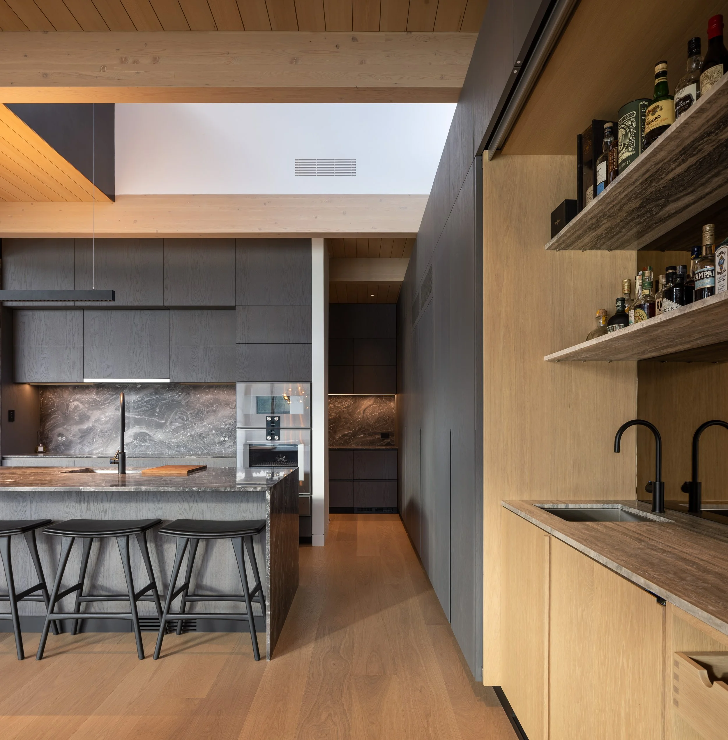 A minimalist Whistler kitchen with integrated cabinetry, stone countertops, and a sculptural island that anchors the space beneath skylit timber beams. This custom home by Durfeld Constructors, with architecture by Burgers Architecture, highlights pr