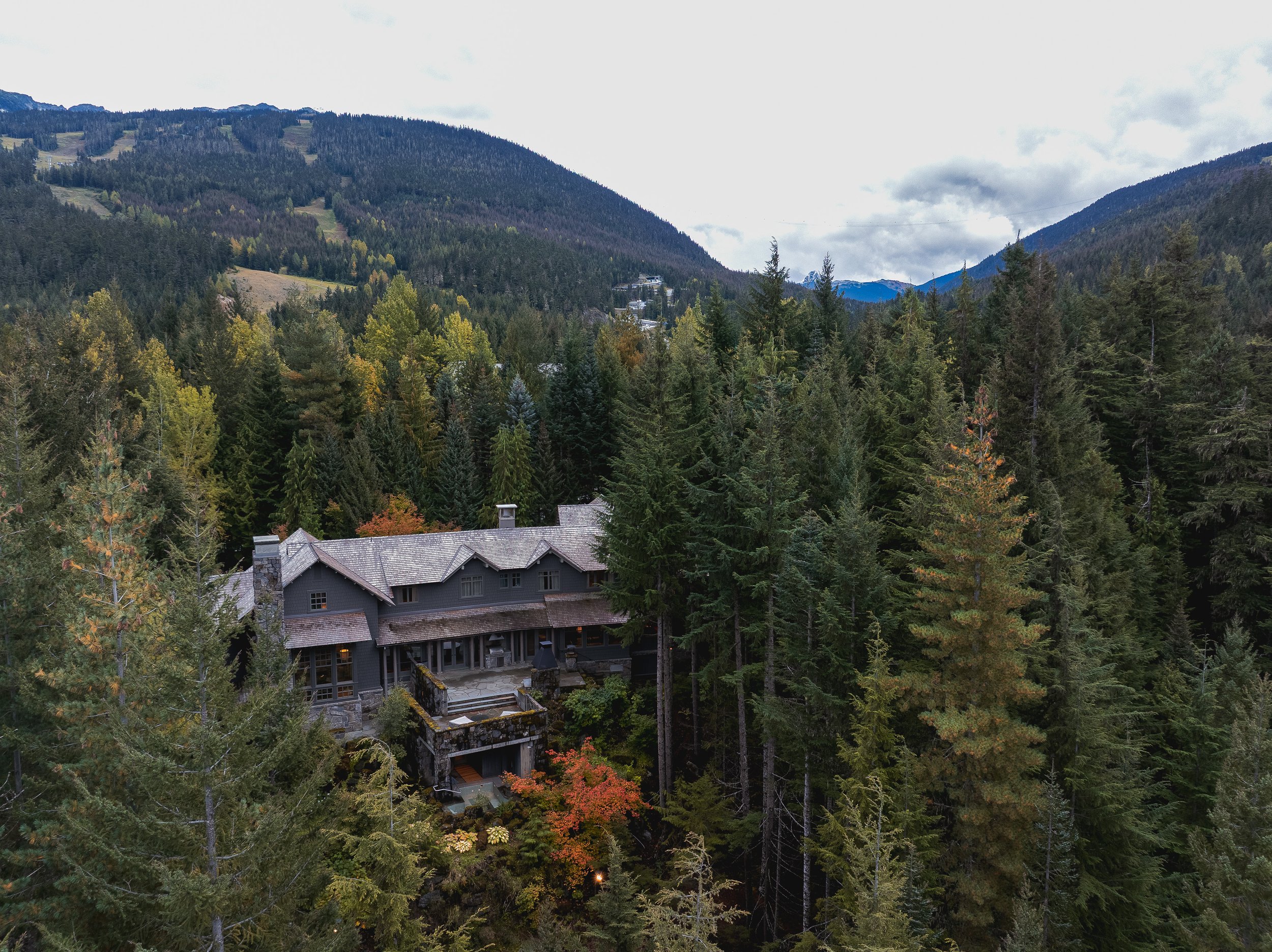 Wide aerial of a Whistler residence surrounded by forest with mountain views in the background.