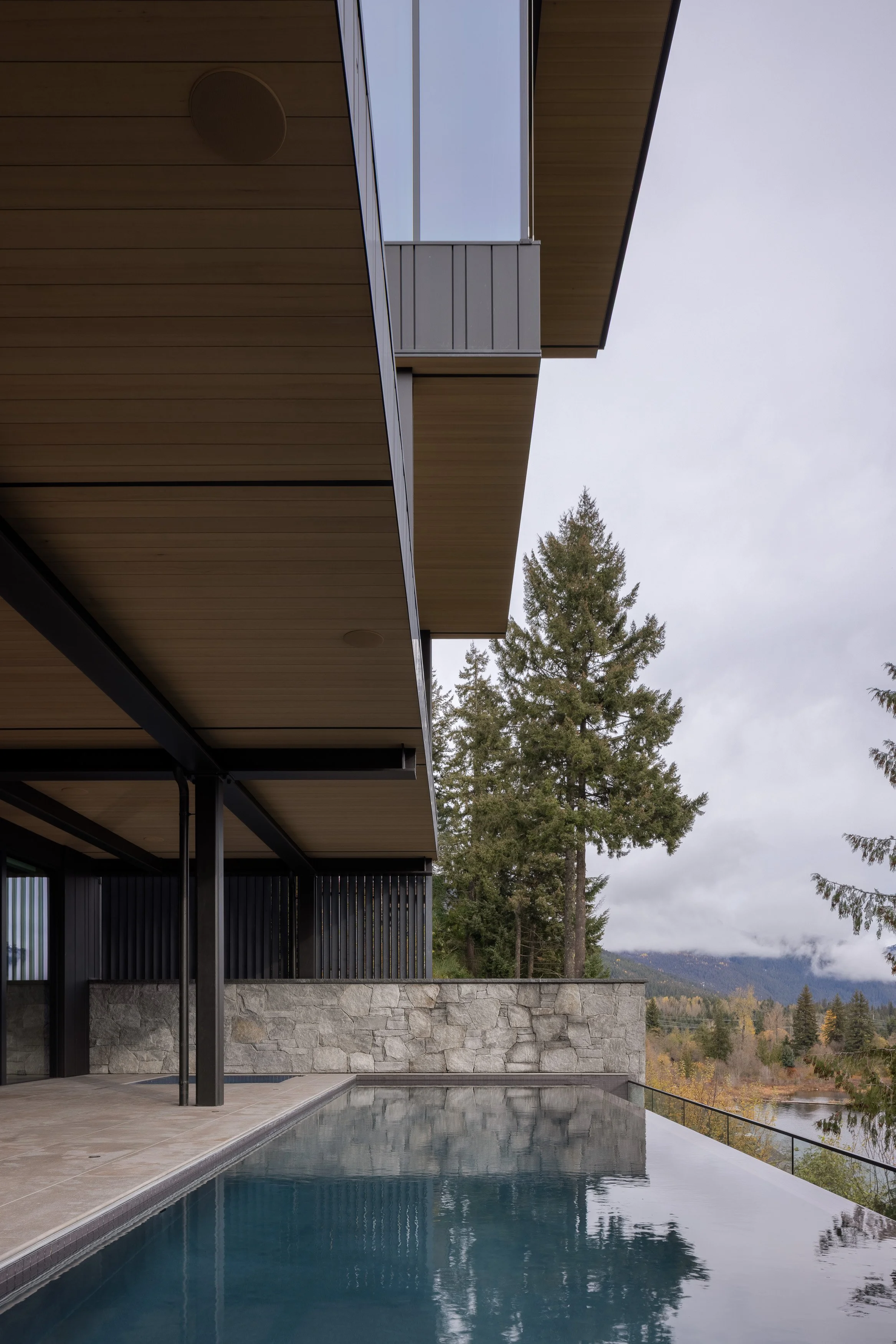 An exterior view emphasizing the home’s layered rooflines, stone walls, and infinity-edge pool set against a forested Whistler backdrop. Designed by Burgers Architecture and built by Durfeld Constructors, the architecture balances strong geometry wit