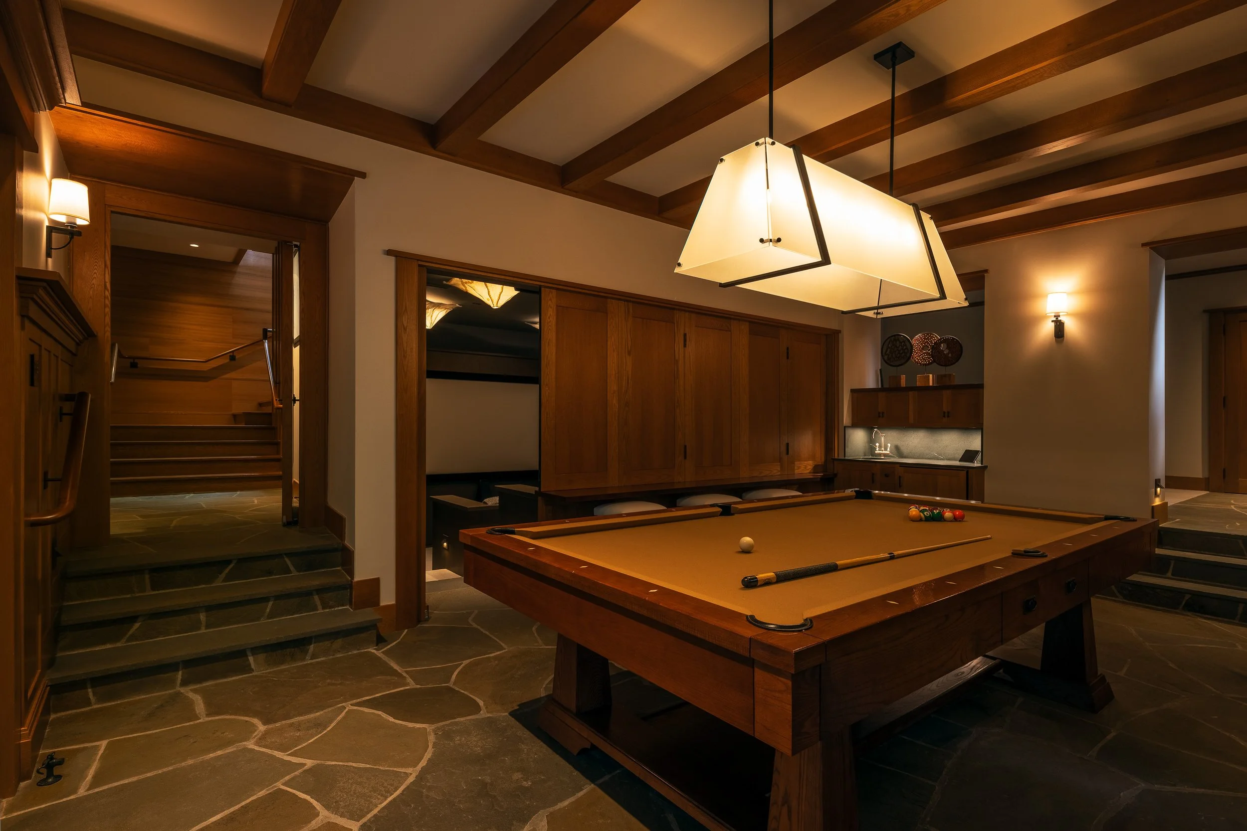 Games room with a pool table, slate flooring, and timber beams lit by modern pendant fixtures in a Whistler home.