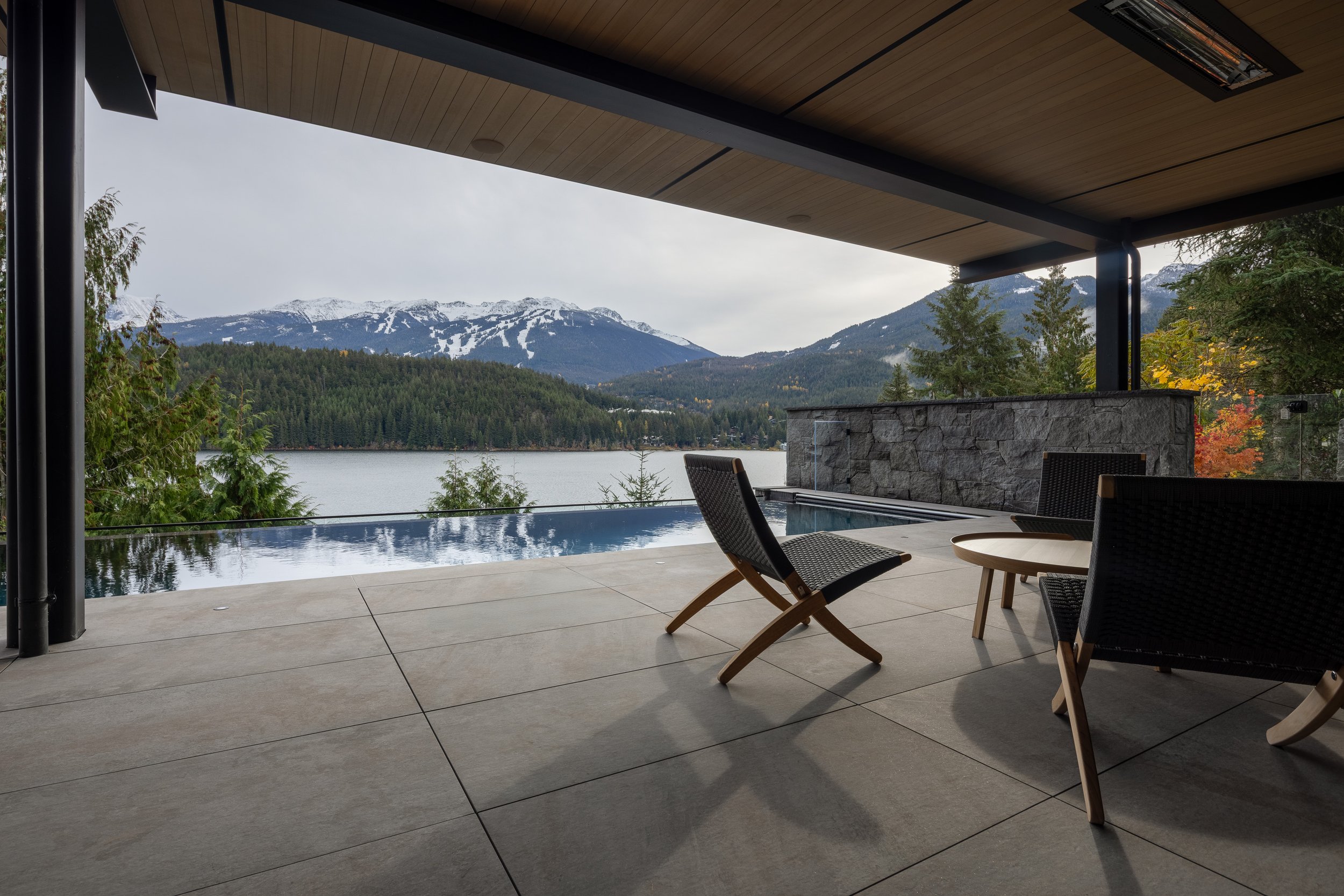 A covered outdoor terrace overlooking the lake and mountains, featuring an infinity-edge pool and refined outdoor furnishings. Built by Durfeld Constructors and designed by Burgers Architecture, this Whistler residence seamlessly extends interior liv