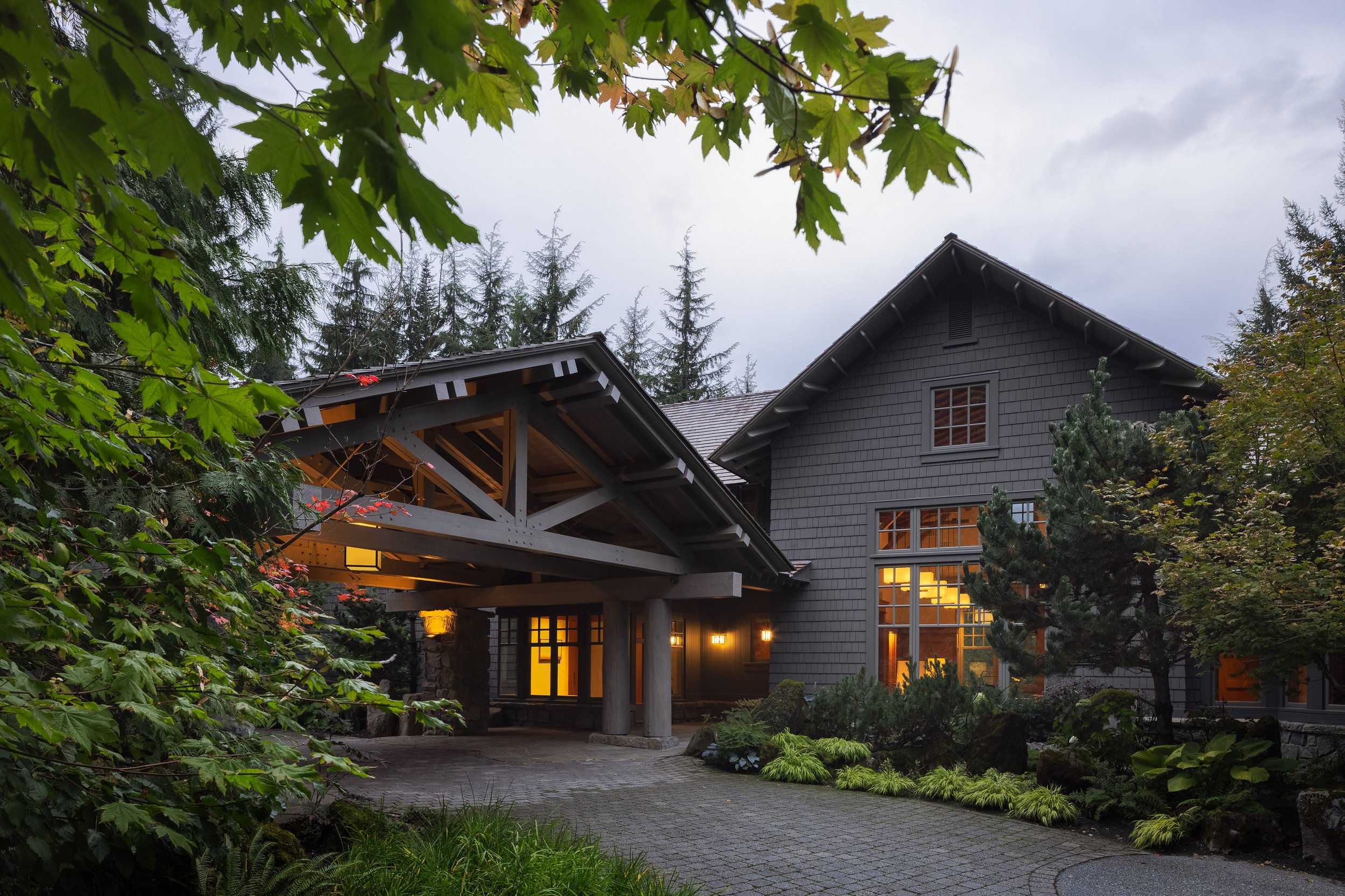Front approach at dusk with covered entry, timber trusses, and landscaped driveway at a Whistler residence.