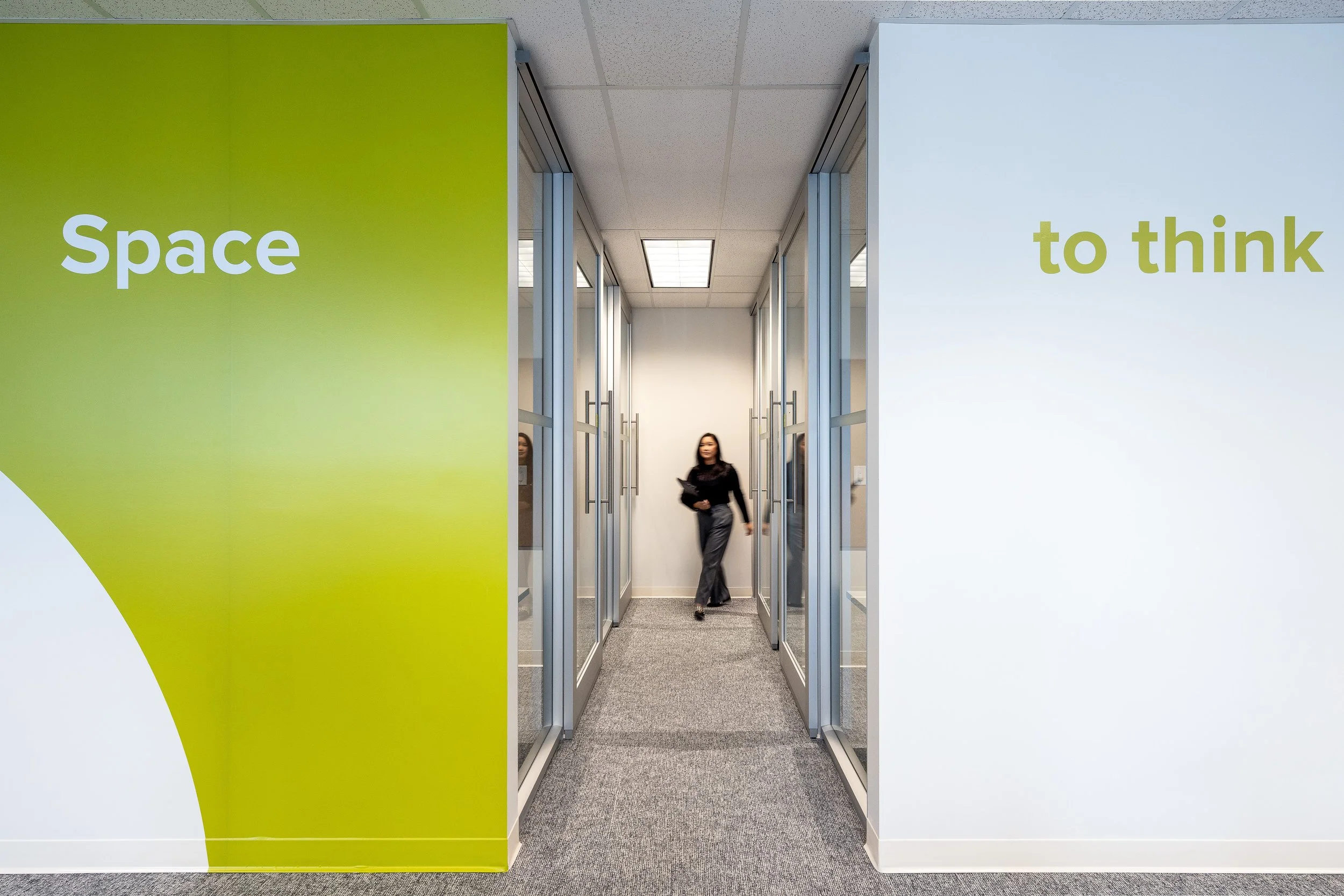 Glass-fronted meeting rooms and corridor with graphic wall signage at the Mott MacDonald Vancouver office.