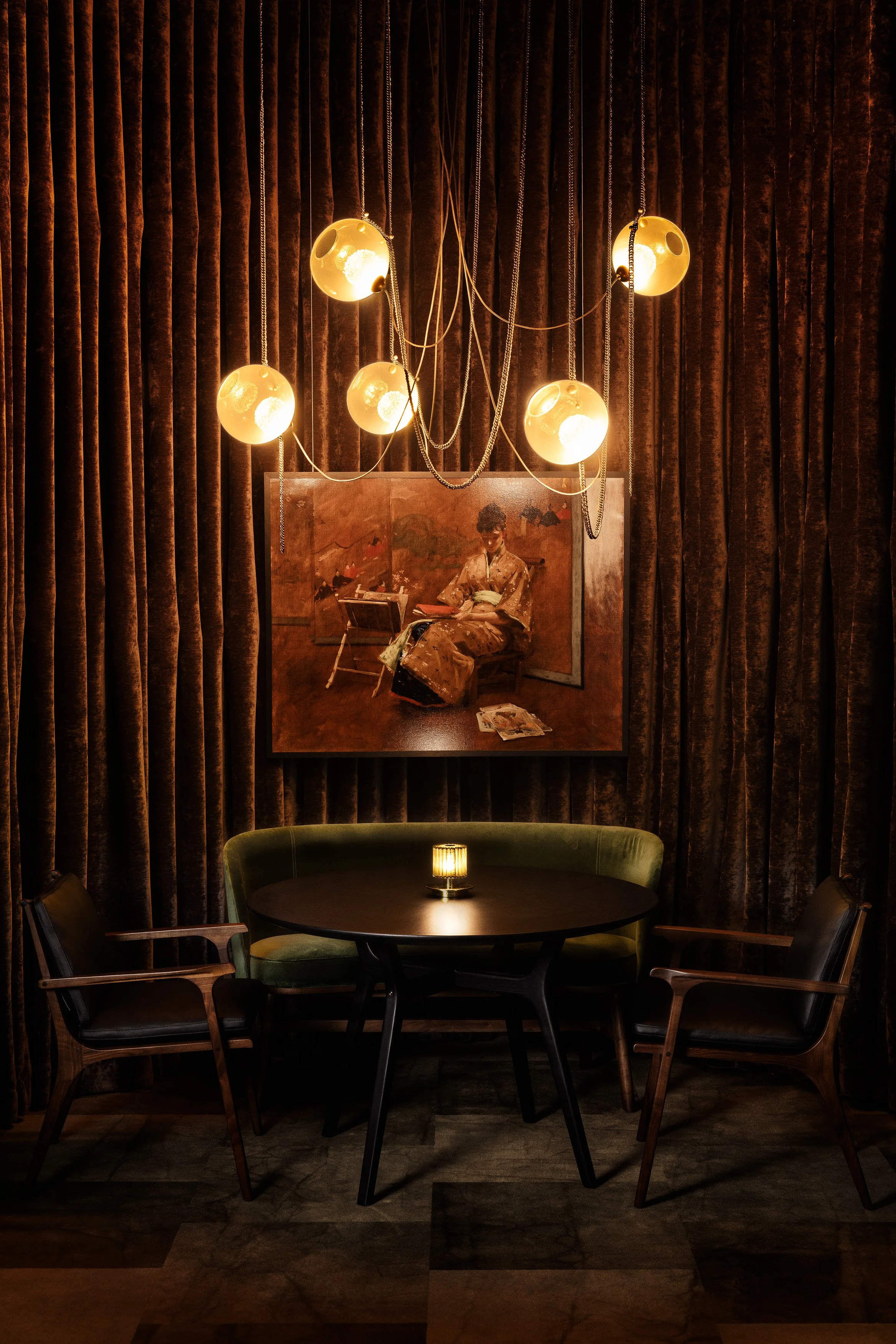 Dining nook with green banquette, round table, framed artwork, and warm globe pendants in the Lightform showroom.