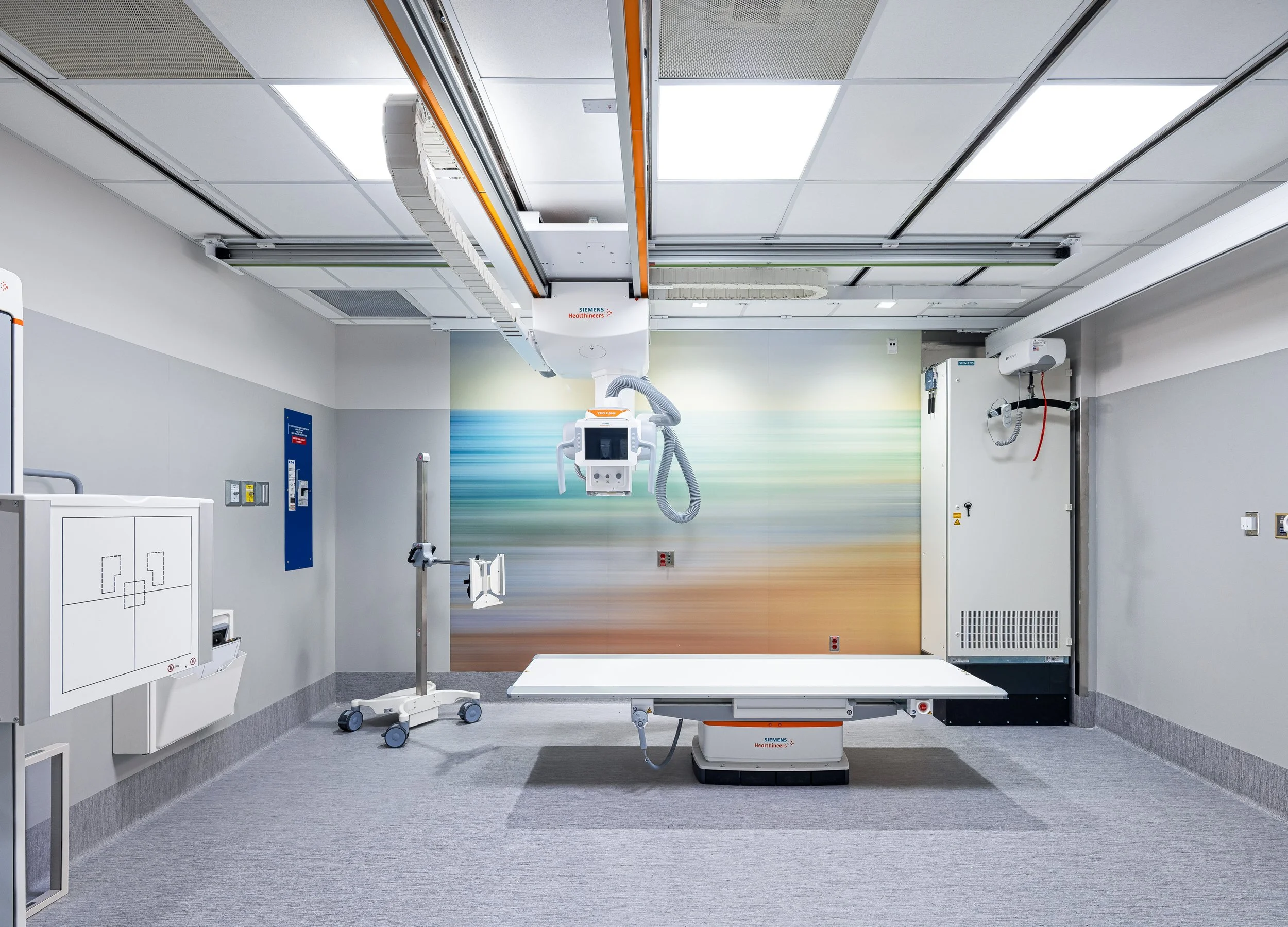 A wide view of the newly completed X-ray room at Vancouver General Hospital, showcasing a clean, highly controlled clinical environment. The design emphasizes efficiency and clarity through integrated medical imaging equipment, seamless wall finishes