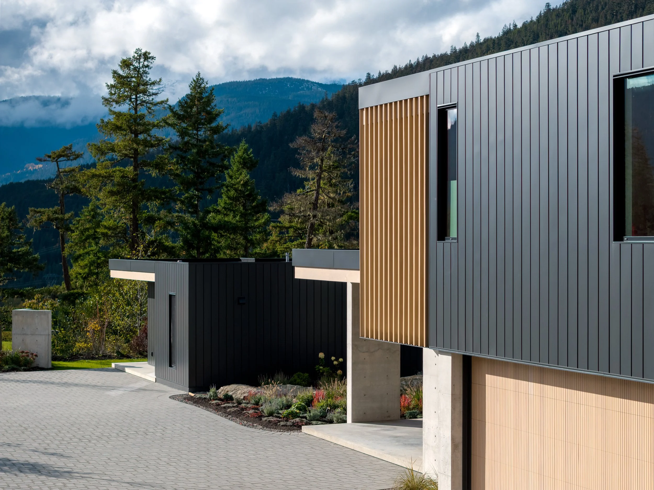 A side elevation showcasing vertical wood screening, concrete structure, and minimalist detailing against a mountainous backdrop. This image emphasizes material contrast and the restrained modern language of the home’s exterior architecture.