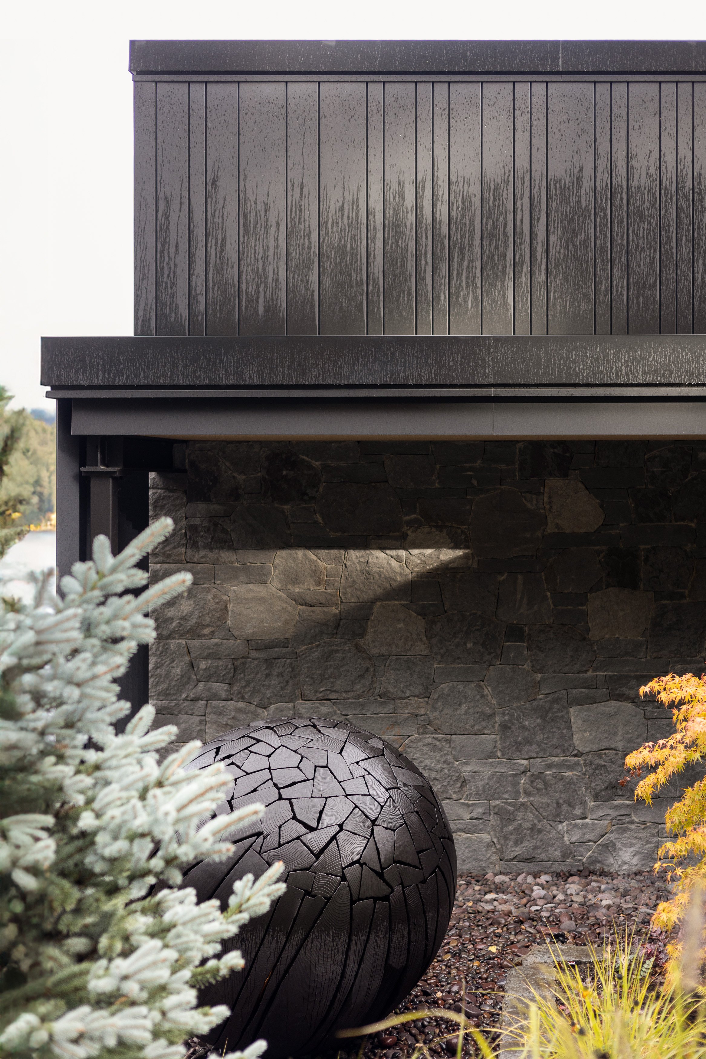 An exterior architectural detail showcasing charred wood cladding and stonework within a landscaped Whistler setting. Built by Durfeld Constructors with architecture by Burgers Architecture, the materials are selected to age naturally in a mountain e