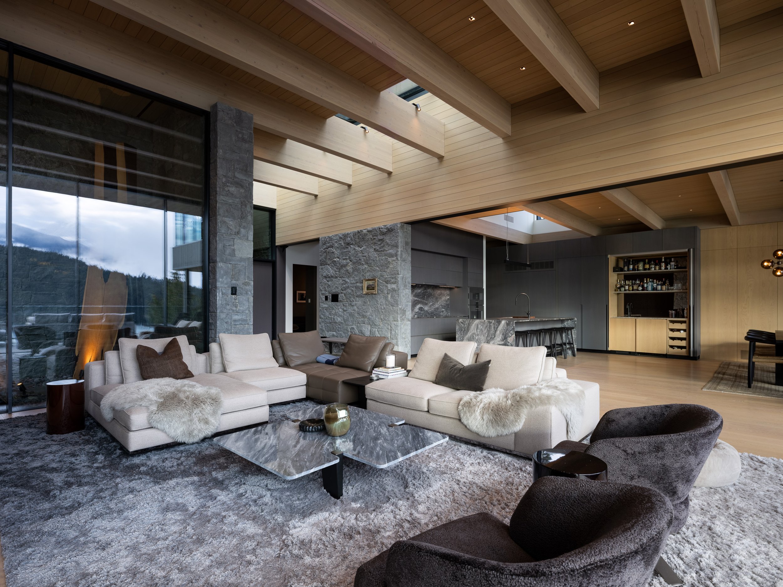 A warm, open-concept living area showcasing exposed timber ceilings, stone columns, and carefully curated furnishings. Designed by Burgers Architecture and built by Durfeld Constructors, this Whistler home demonstrates how natural materials create a 