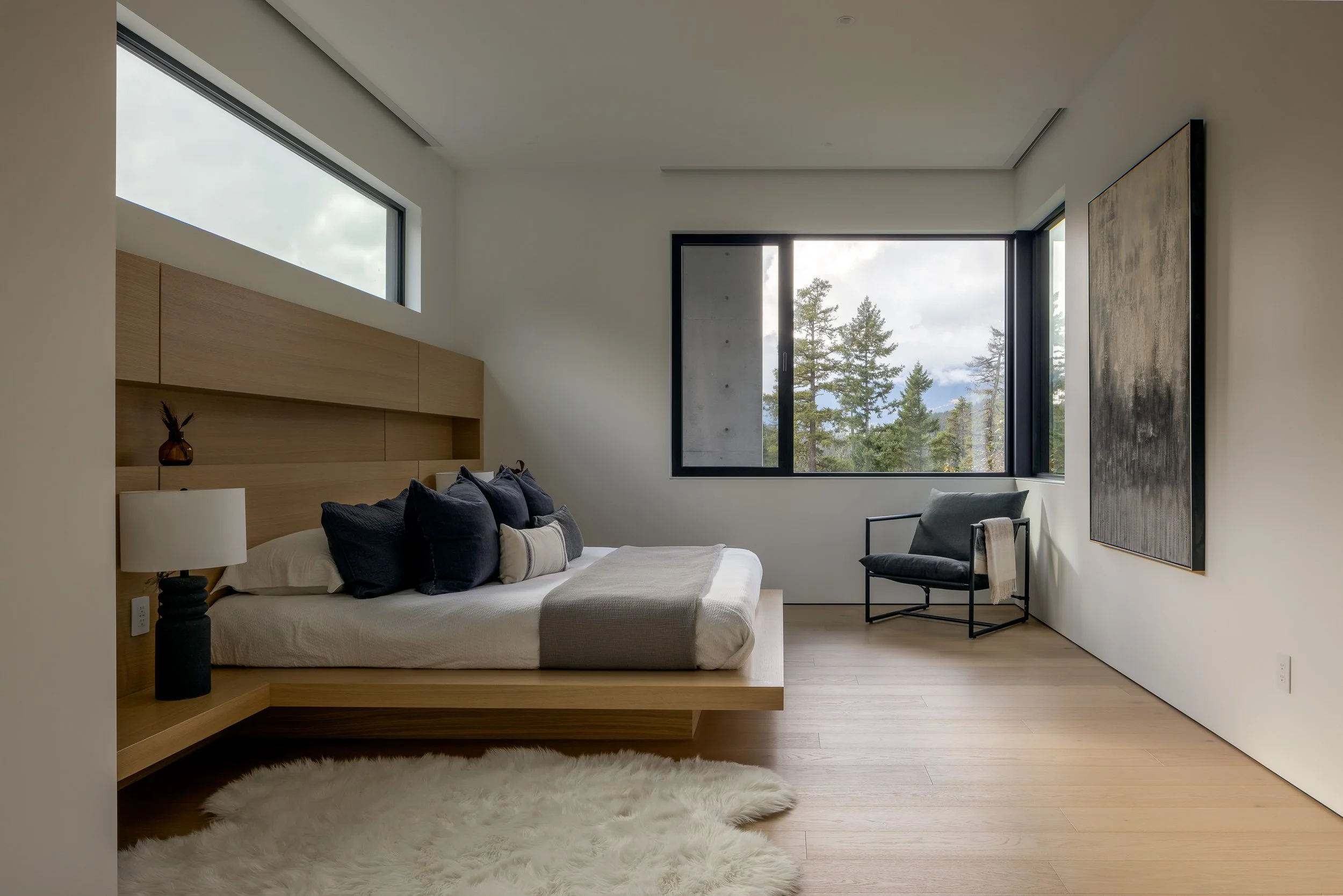 A minimalist bedroom interior with integrated wood millwork, soft natural light, and framed forest views. This space reflects a calm, restrained approach to residential interior architecture.