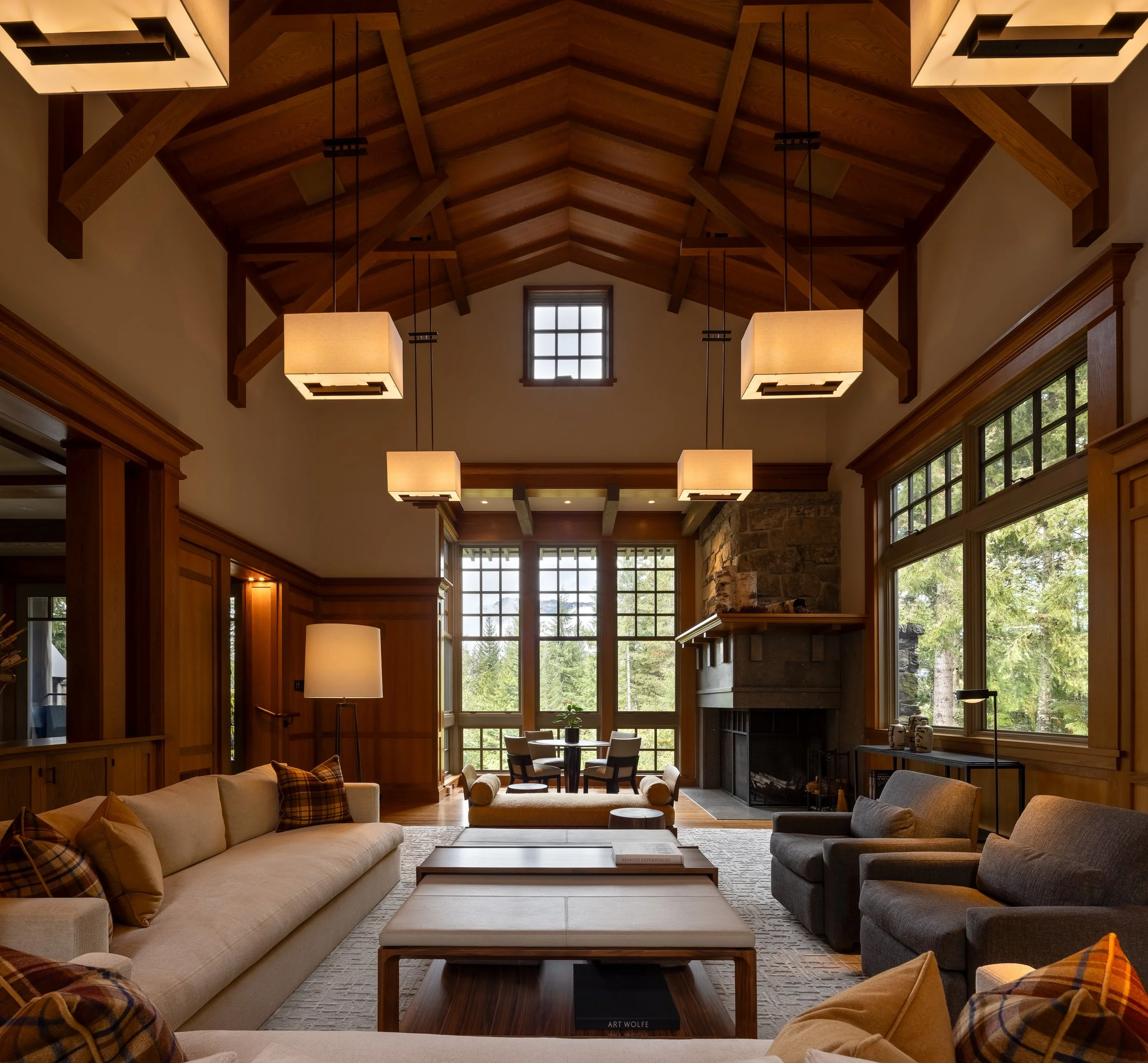 Vaulted great room in a Whistler home with timber beams, stone fireplace, and large windows overlooking the forest.