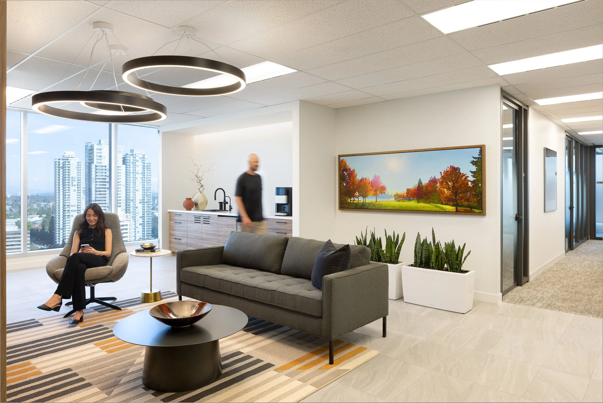 Sun Life office lounge in Burnaby with modern seating, circular pendant lights, city views through large windows, and employees using the space.