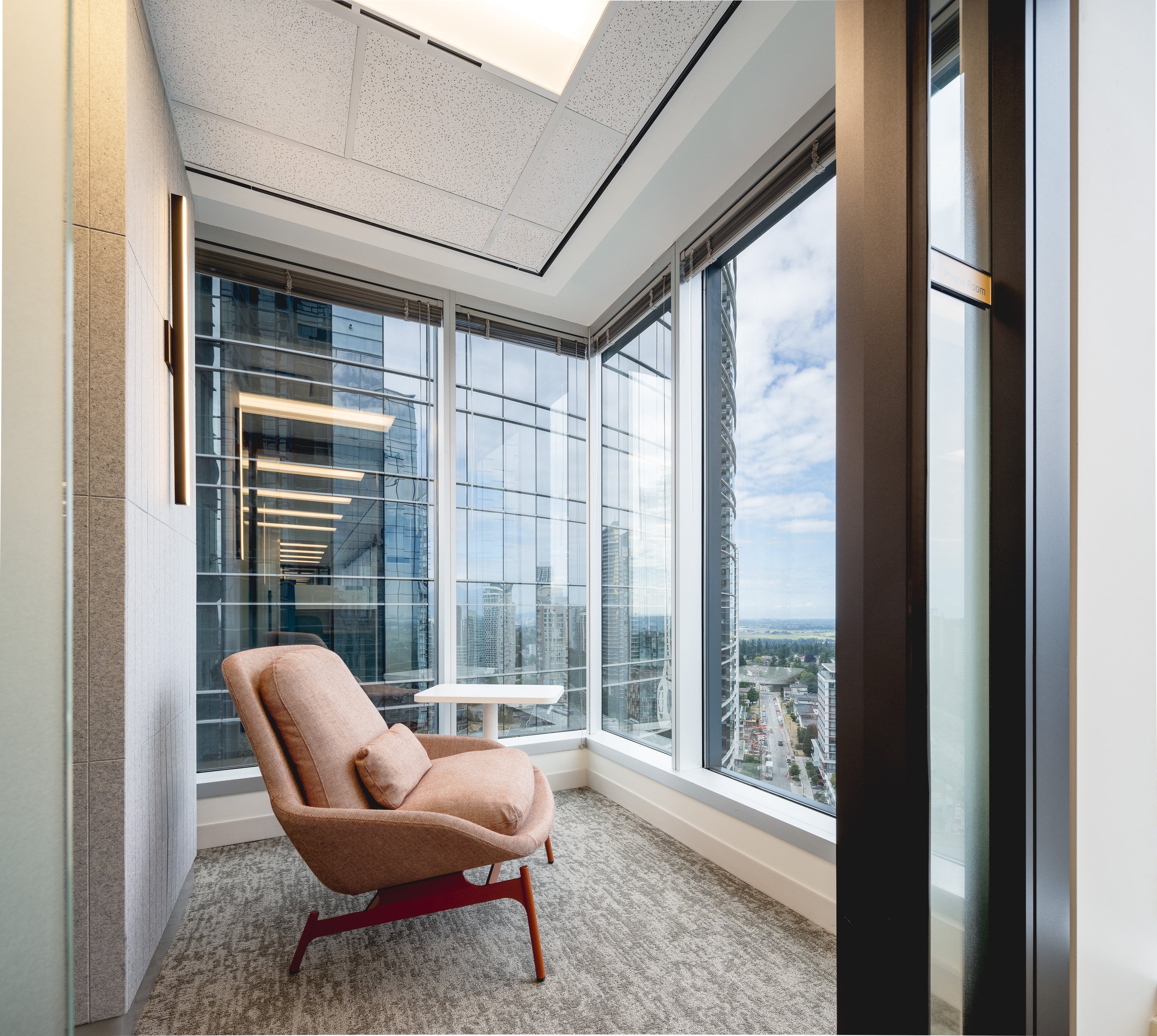 Quiet seating area in the Sun Life office with an upholstered lounge chair positioned beside floor-to-ceiling windows overlooking Burnaby.