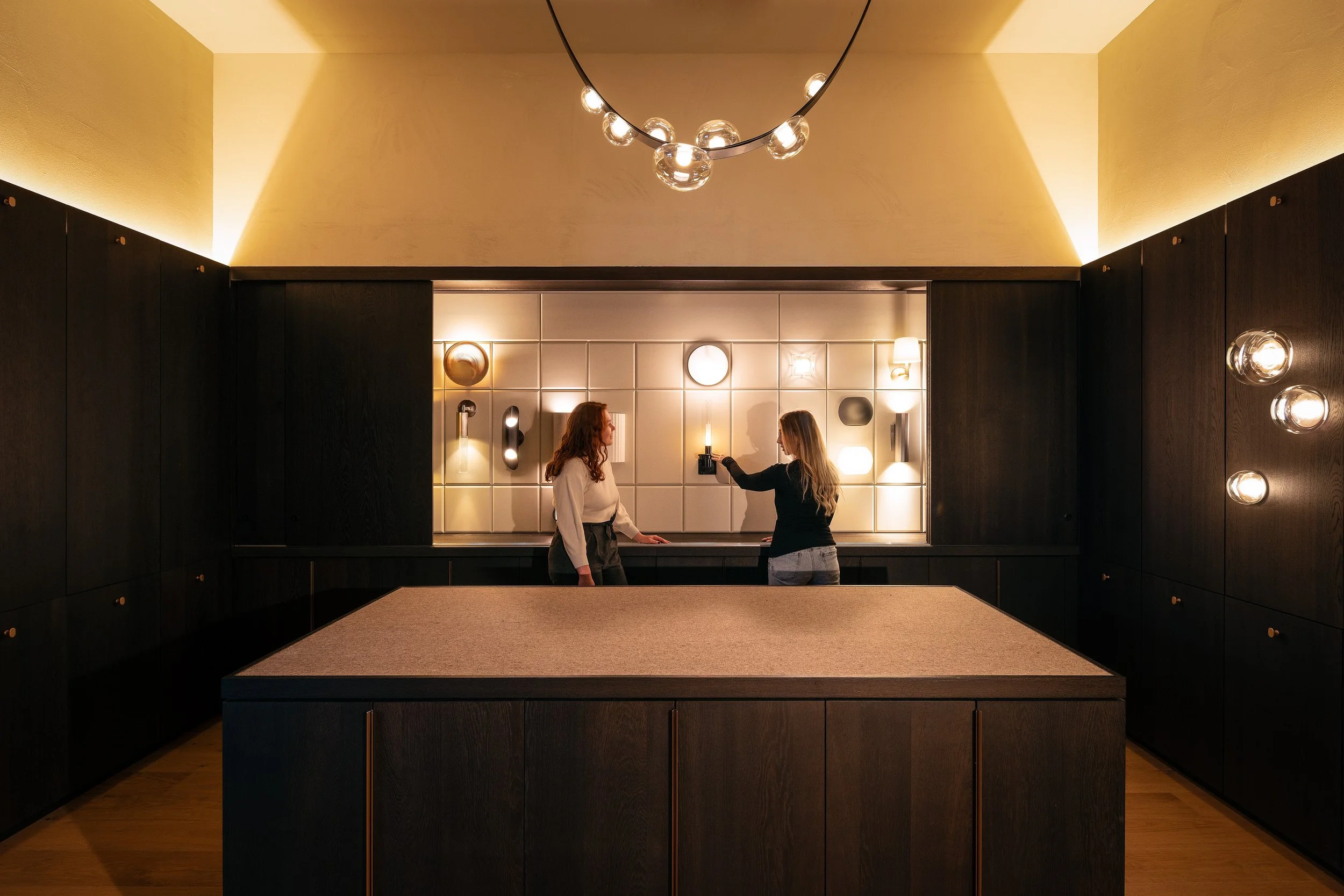 Wide panoramic view of the Lightform Vancouver showroom with a large central island, wall-mounted lighting displays, and two people reviewing fixtures.