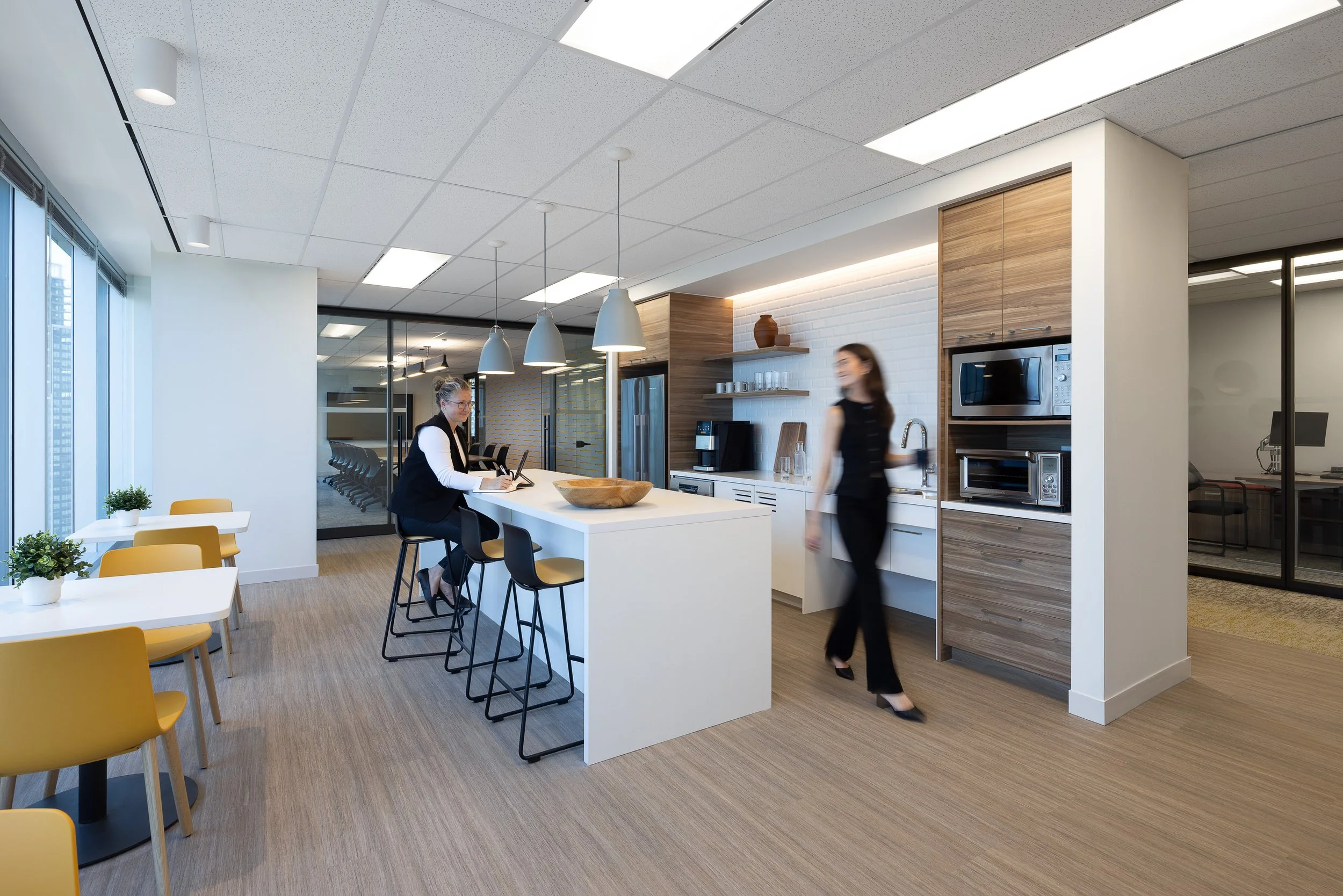 Sun Life office kitchen and collaboration area in Burnaby with a central island, pendant lighting, built-in appliances, and employees using the space.