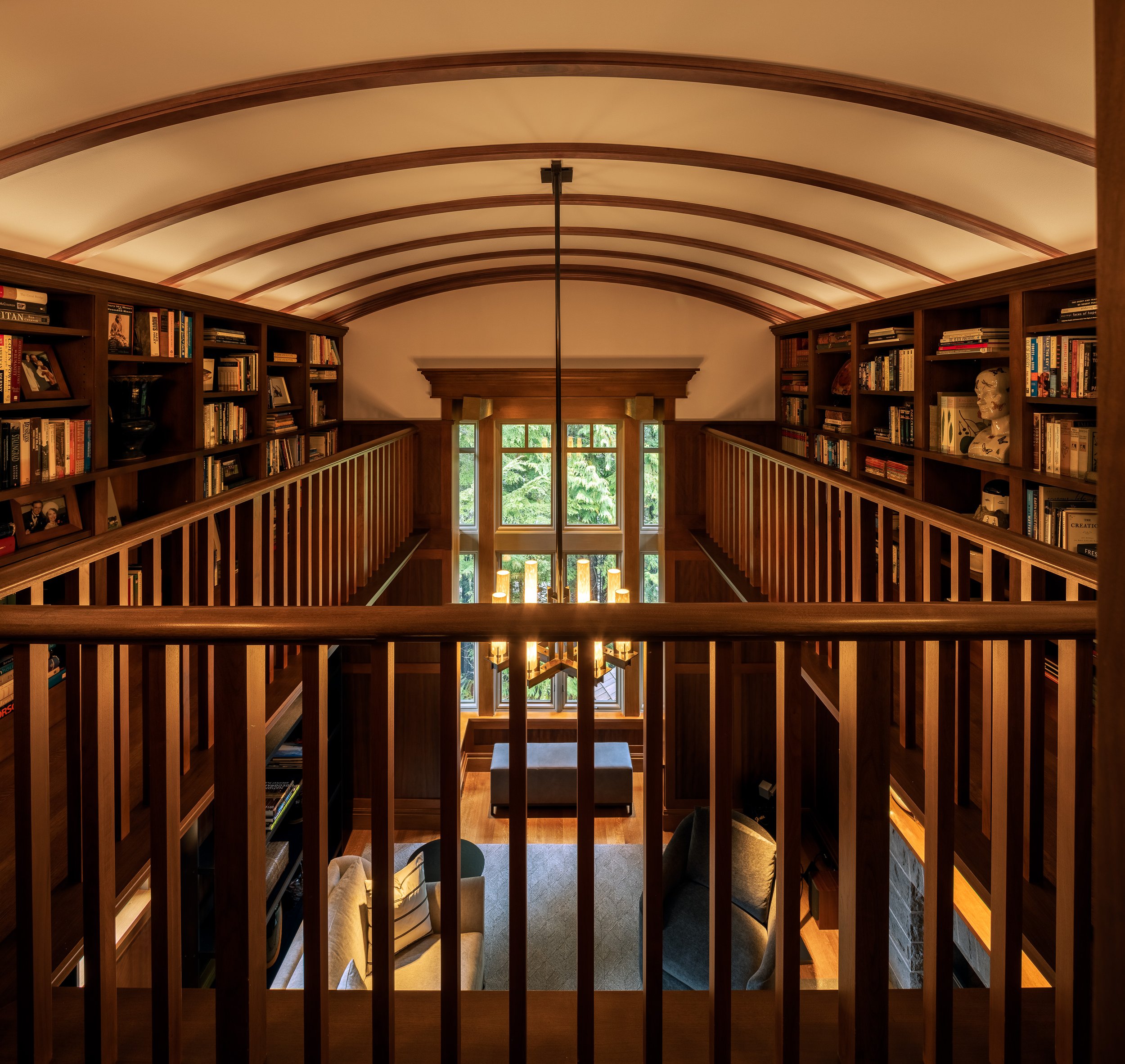 Library mezzanine with built-in bookshelves and wood railings overlooking the living area in a Whistler mountain residence.