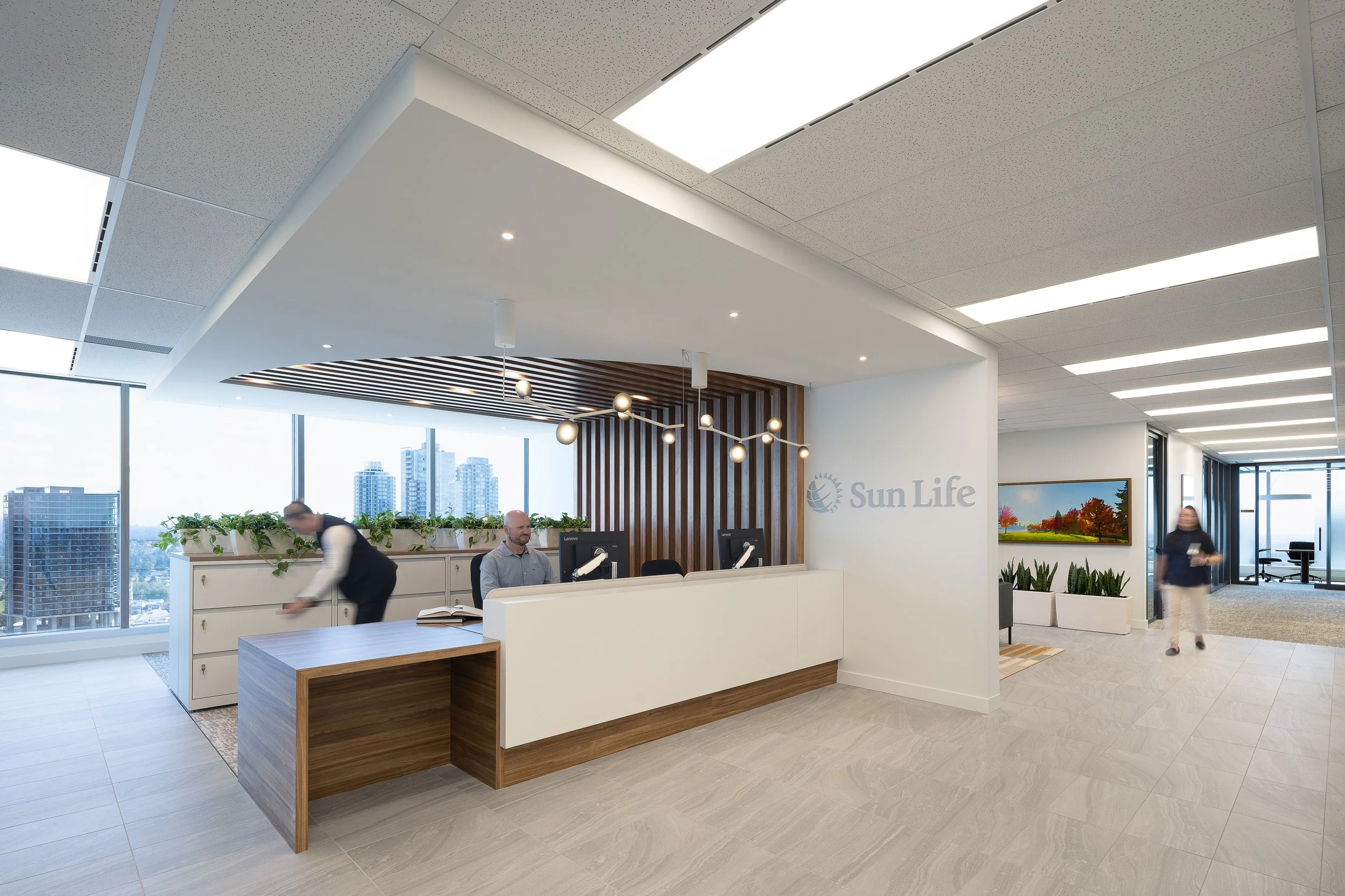 Panoramic view of the Sun Life office reception and lounge area in Burnaby with wood accents, integrated lighting, and city views through floor-to-ceiling windows.