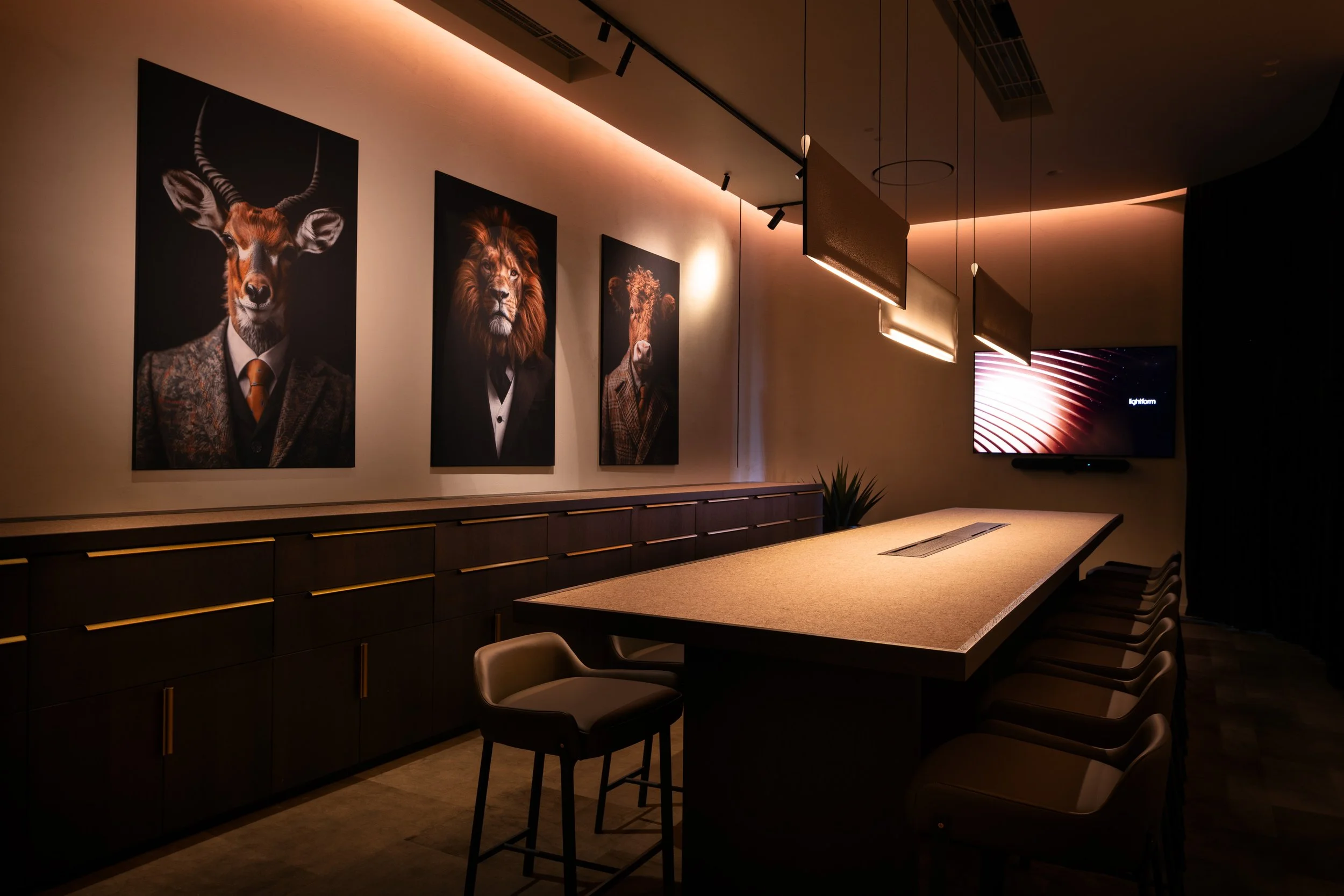 Long meeting table with upholstered chairs beneath suspended linear pendant lights, with framed artwork on the wall in the Lightform showroom.