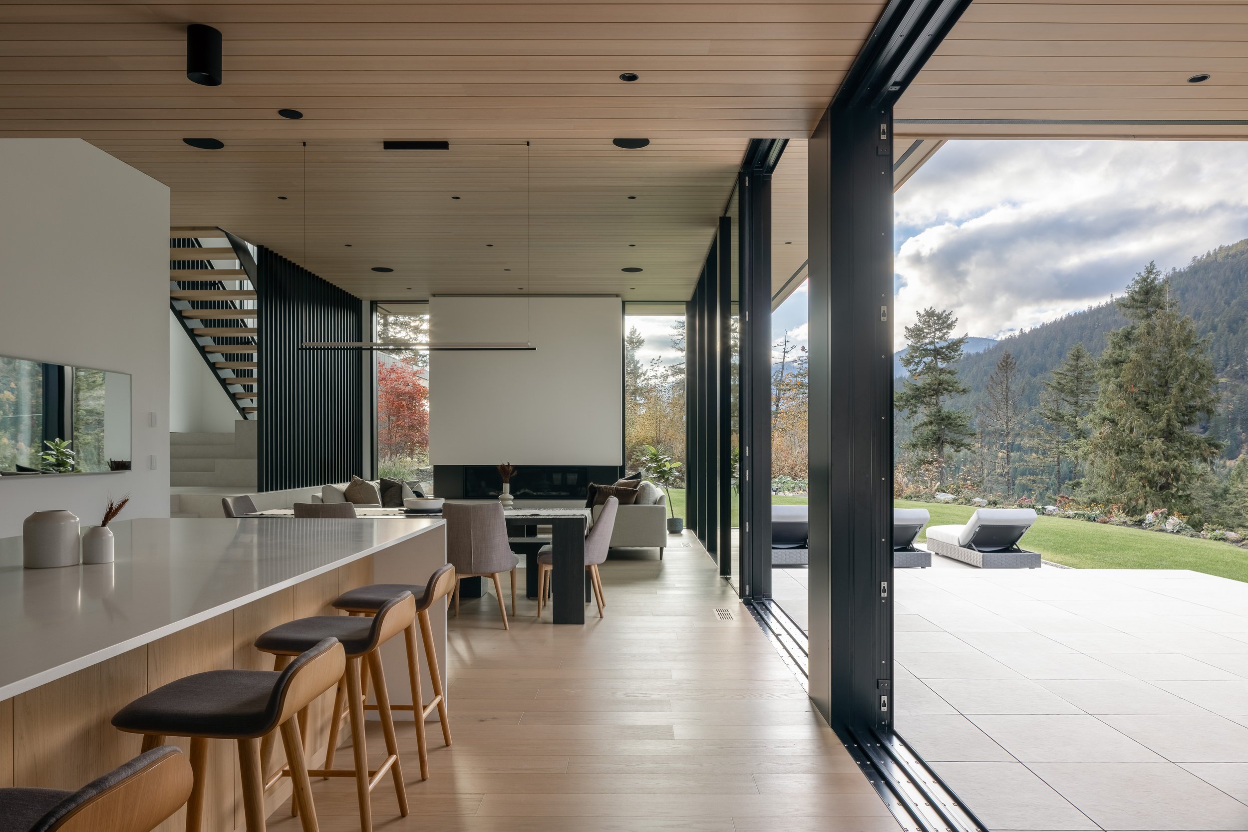 Interior wide looking out: kitchen/island + living/dining, big opening to patio + mountain view.