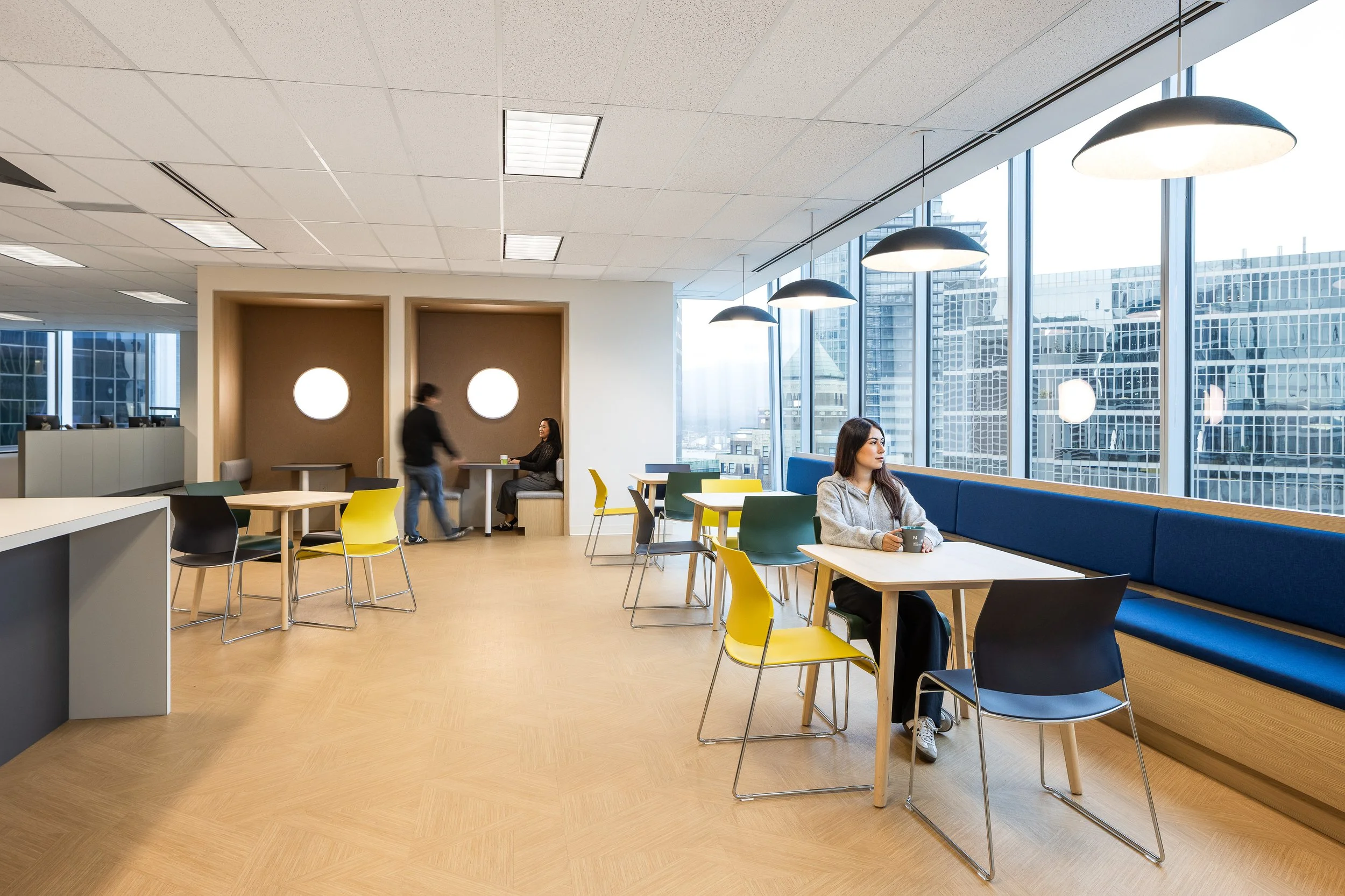 Open collaborative seating area at the Mott MacDonald Vancouver office, featuring floor-to-ceiling windows, built-in banquette seating, and natural wood finishes, designed and built by Aura Office Interiors.