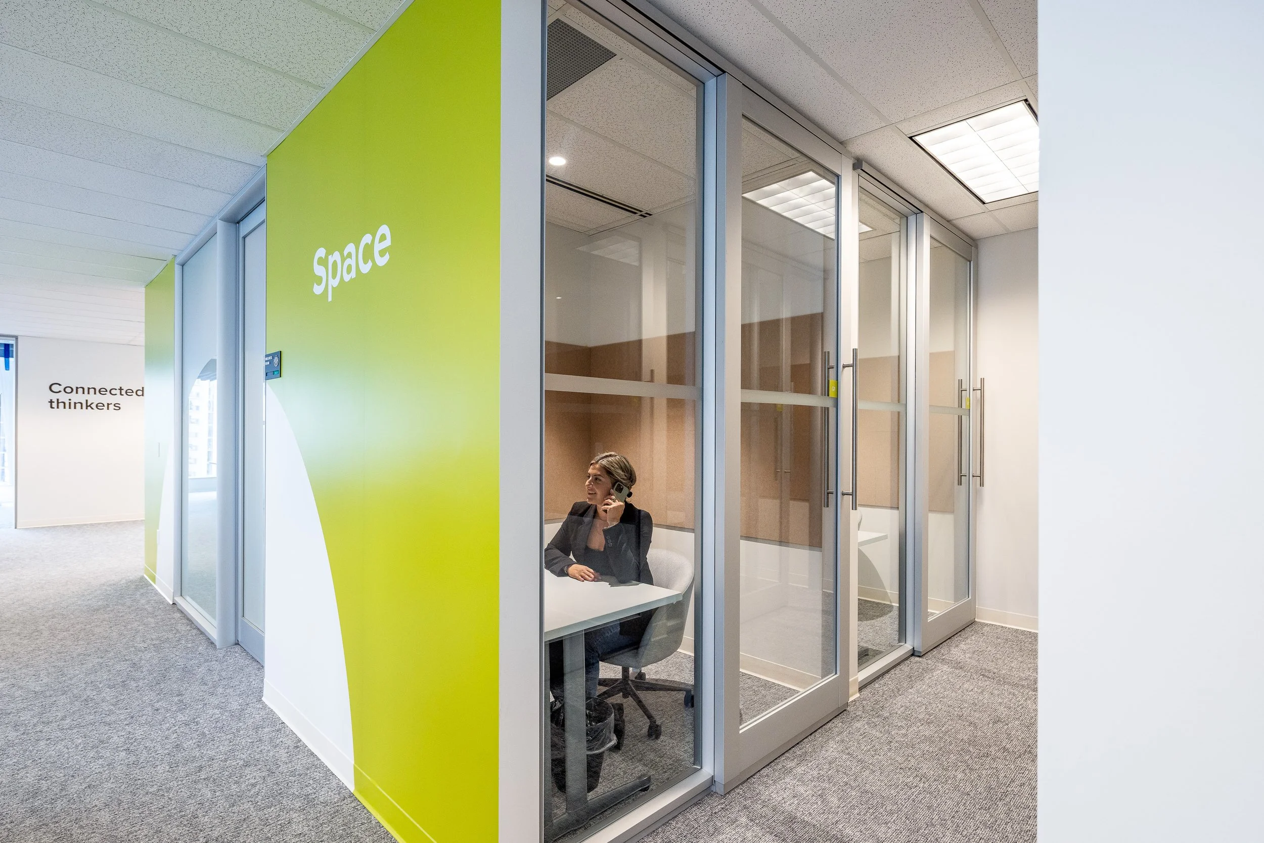 Glass-fronted meeting rooms with green branded wall panels at the Mott MacDonald Vancouver office, designed by Aura Office Interiors.