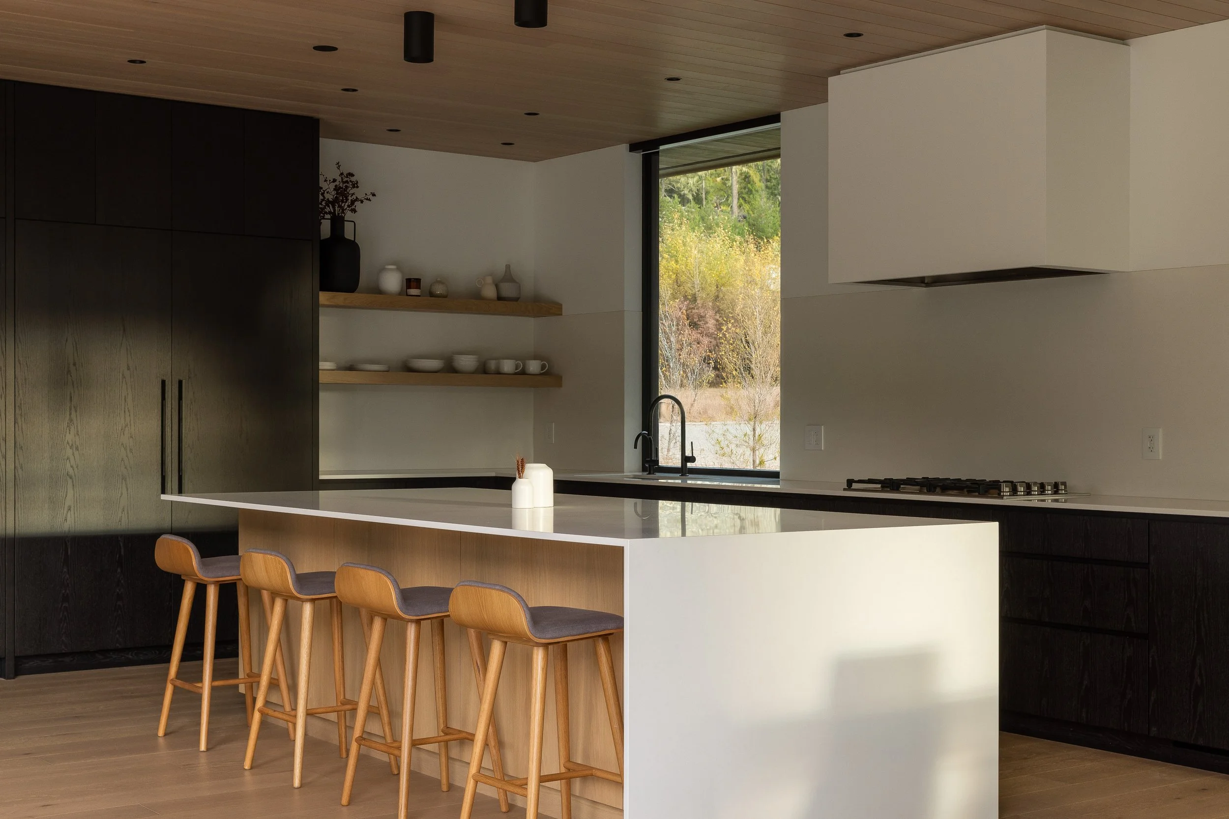 Kitchen (horizontal): island with stools, warm/late light, shelves + sink window.