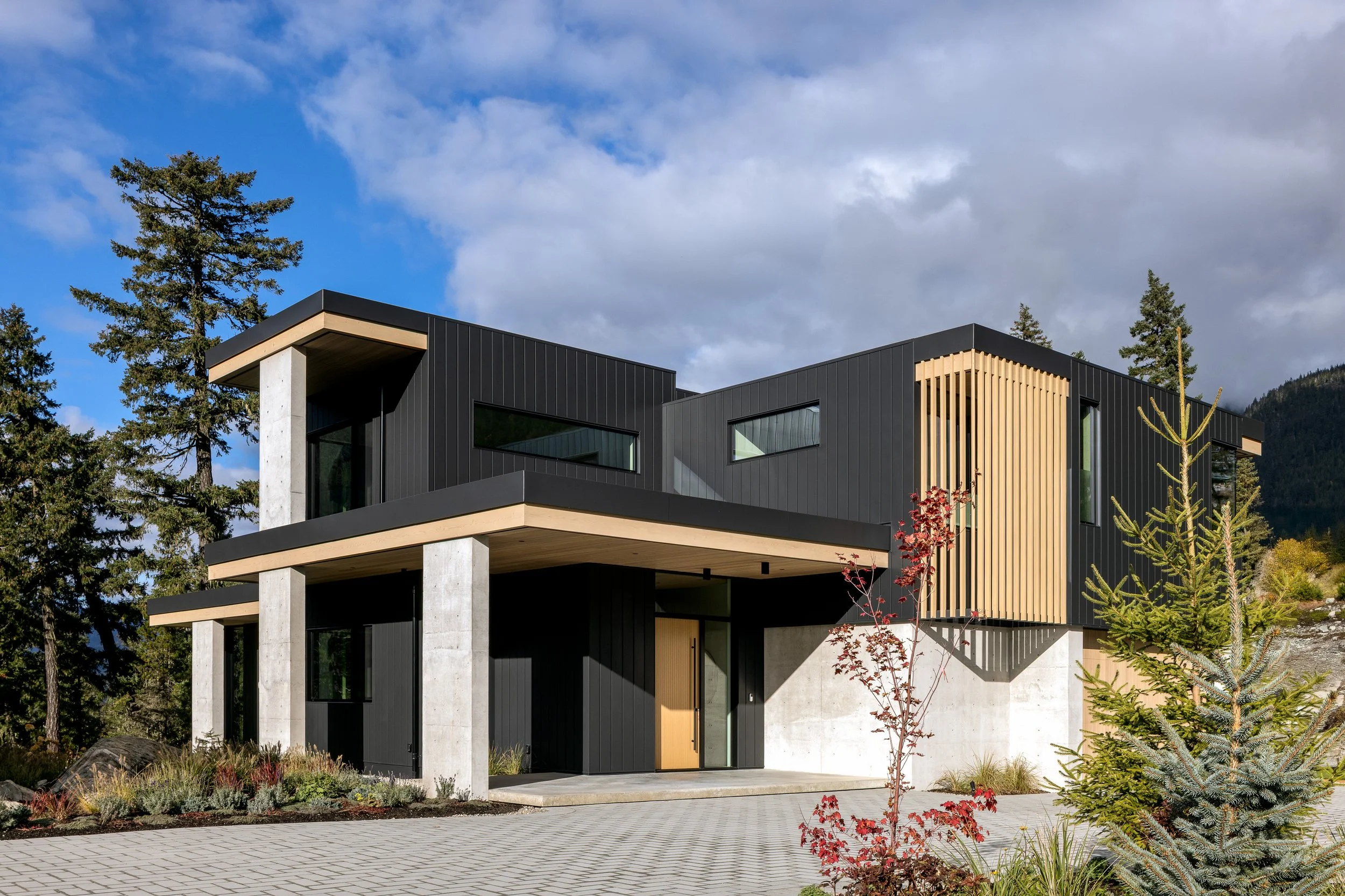 A three-quarter exterior view of the residence showing layered volumes, concrete supports, and landscaped surroundings. This image captures the balance between modern architectural form and the mountain environment.