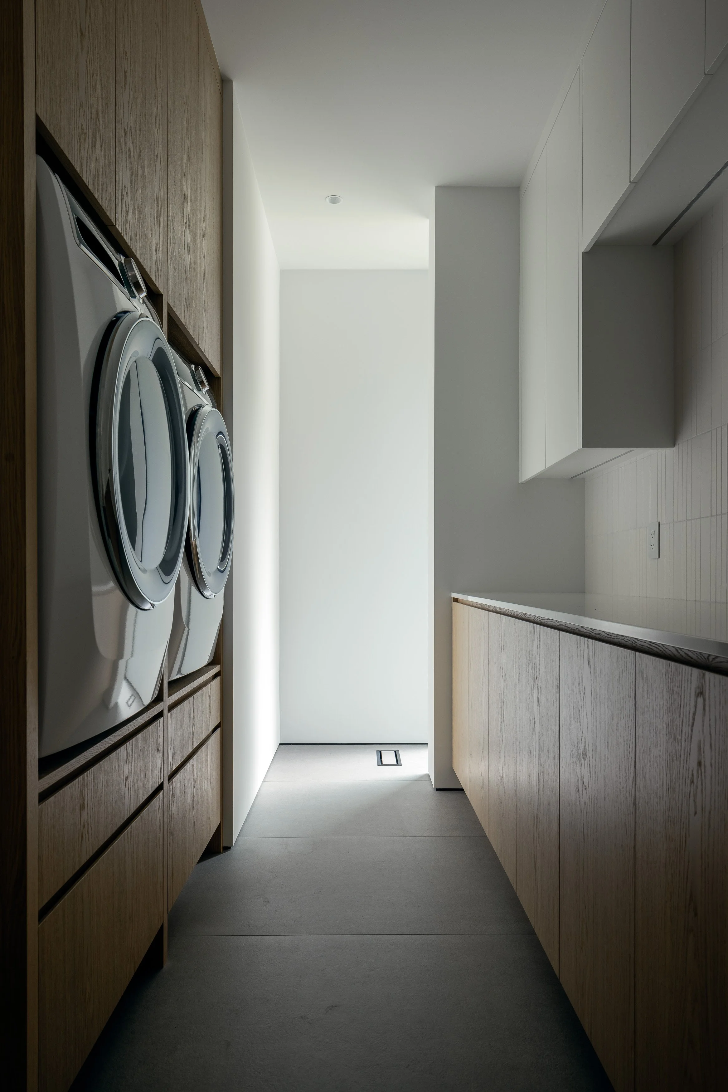 A compact utility and laundry space featuring integrated cabinetry, concealed appliances, and a refined neutral palette. This image highlights functional residential design executed with architectural clarity.