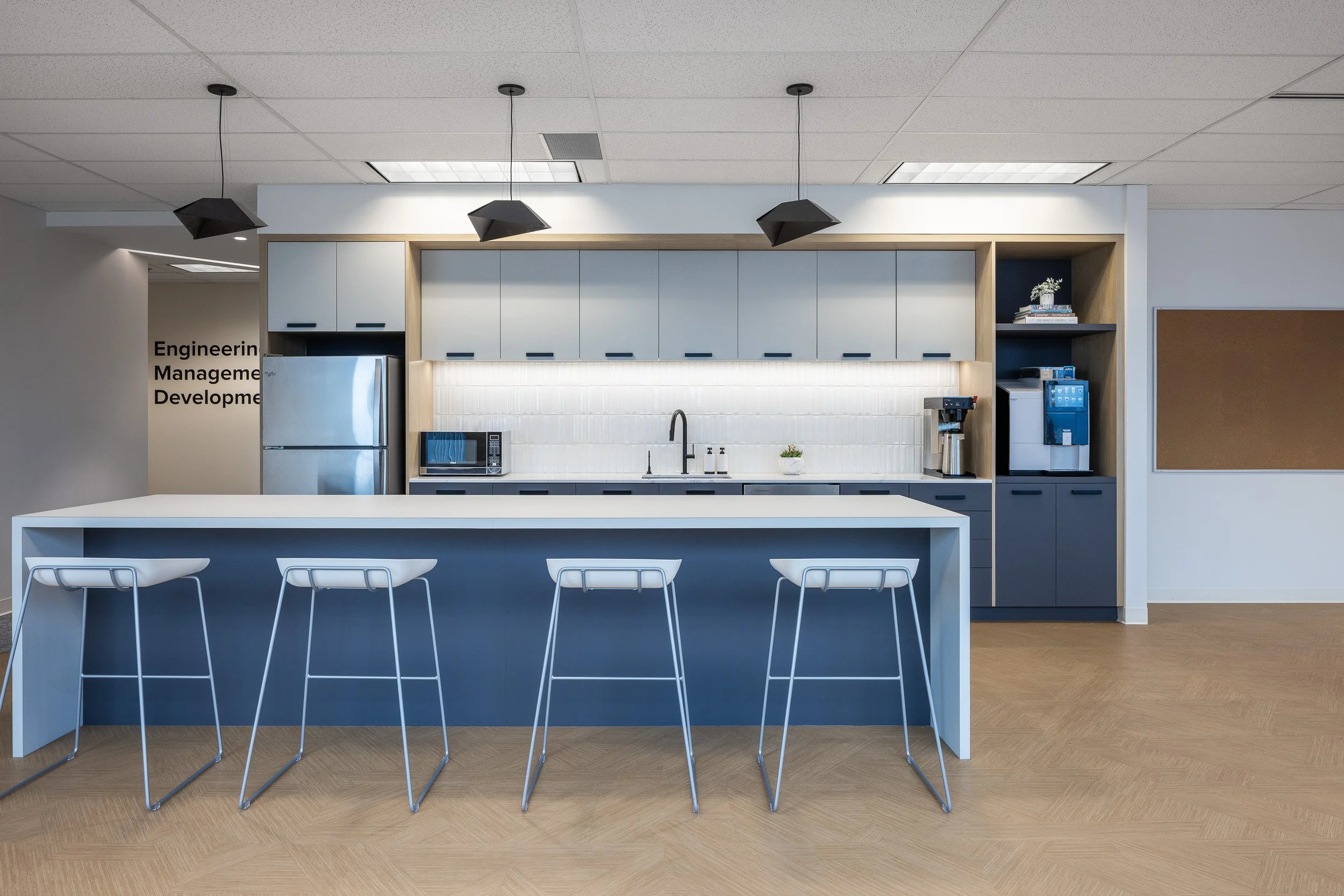 Office kitchen and social hub at the Mott MacDonald Vancouver office, featuring a large island with stools, built-in cabinetry, and integrated appliances.