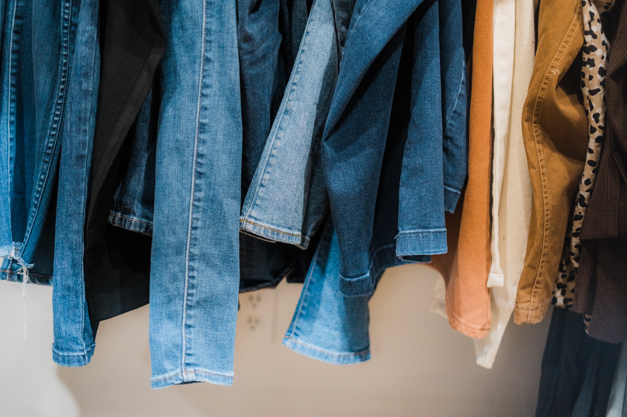 Rack of hanging denim jeans and various colored pants