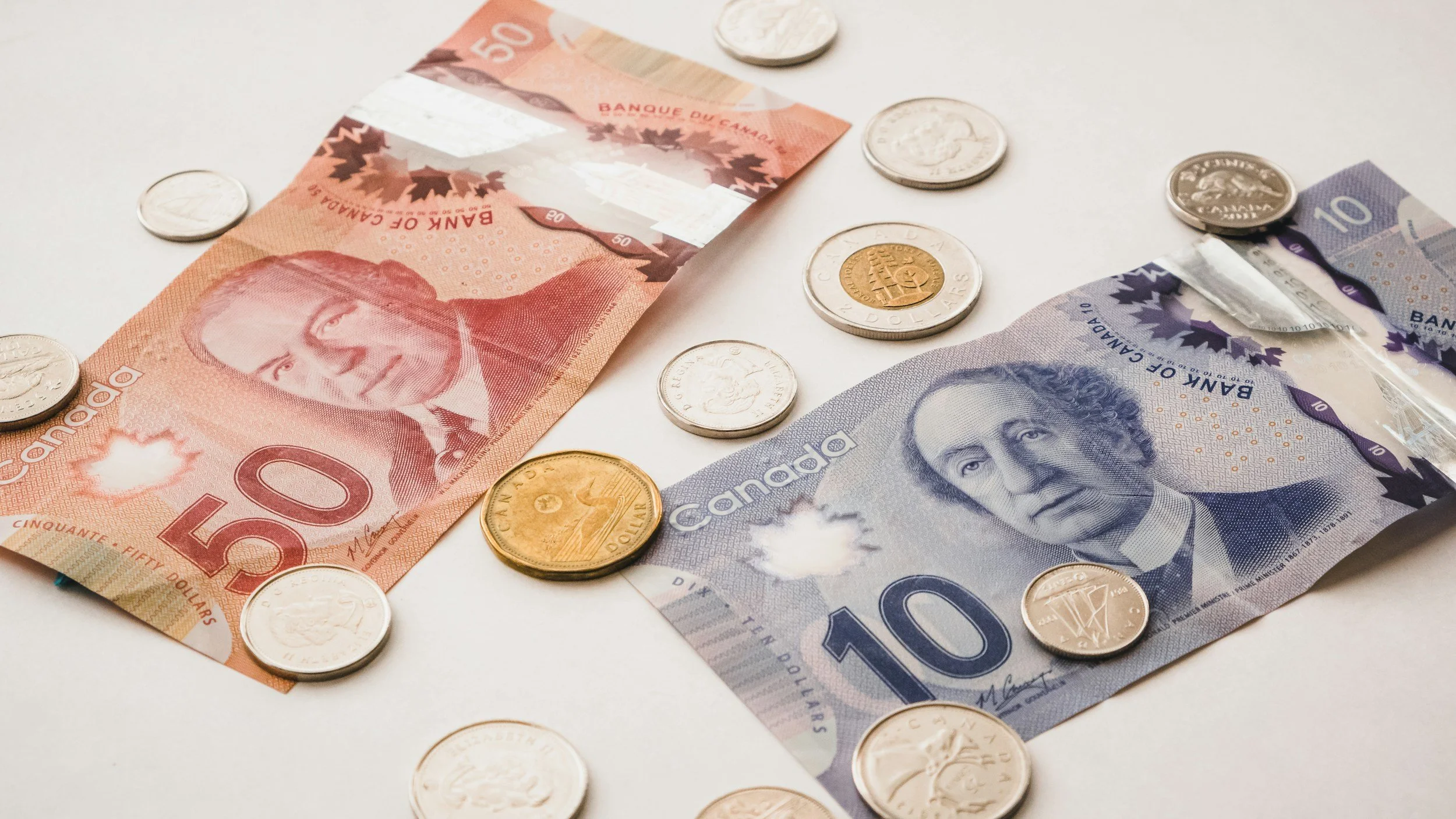 Canadian banknotes of 50 and 10 dollars along with various coins laid out on a white surface.
