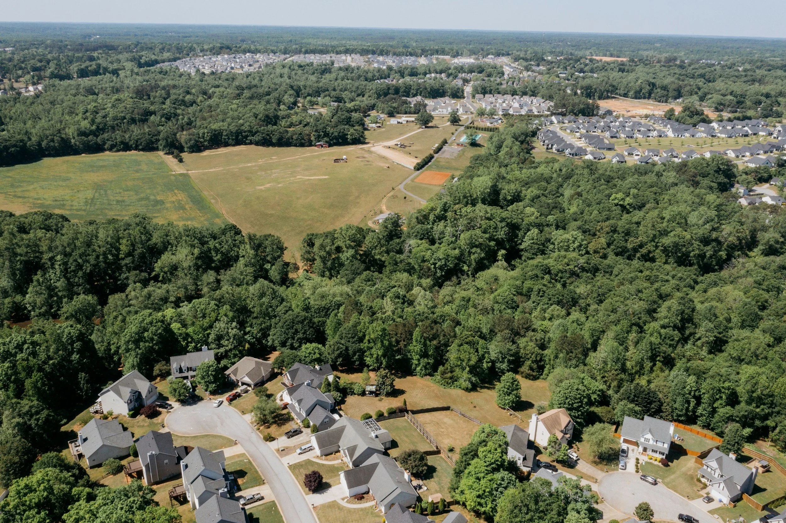 Aerial view of a suburban neighborhood with houses, trees, and open green fields.