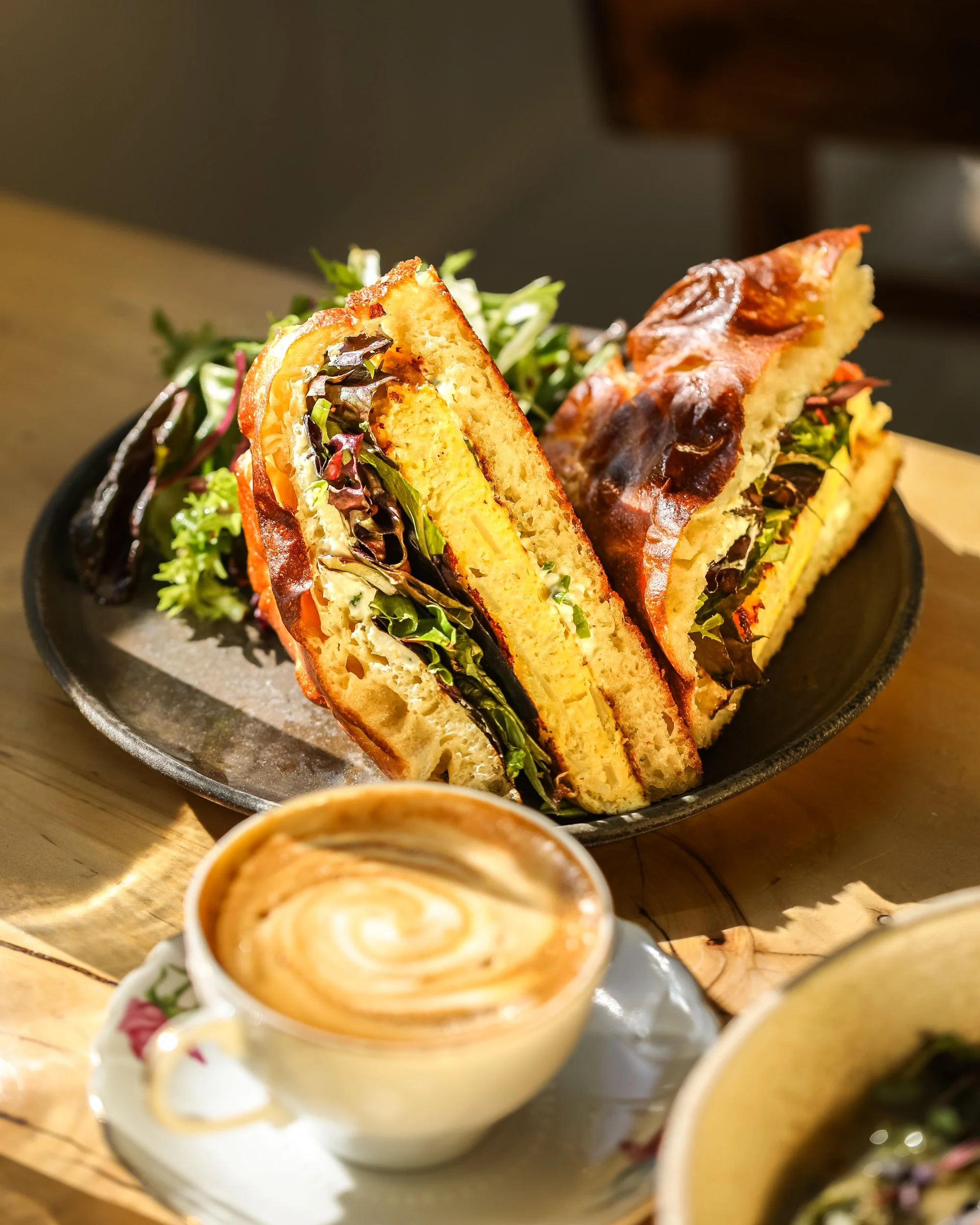 beautifully plated egg frittata sandwich on house made focaccia with a latte in the foreground