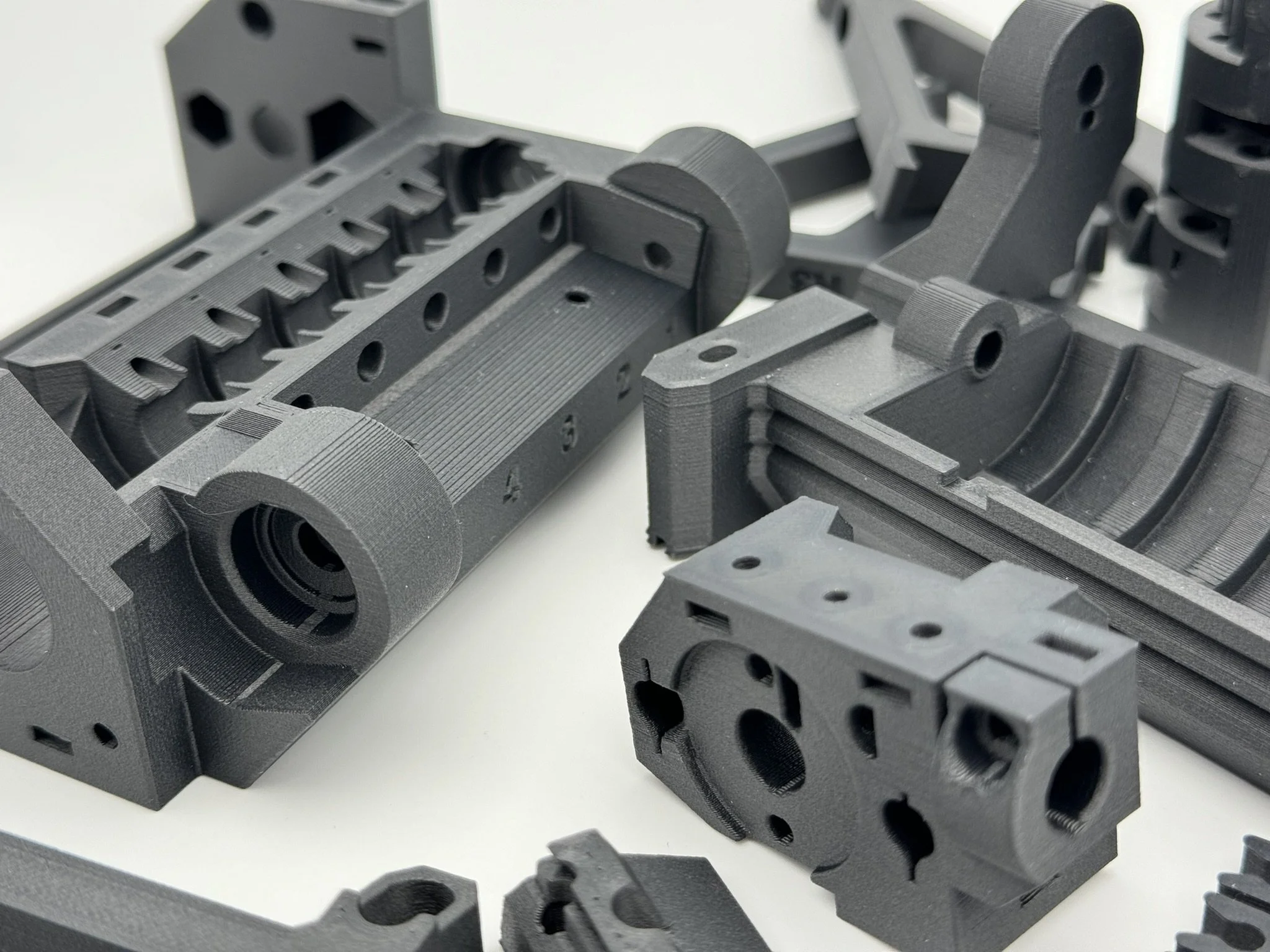 Mehrere schwarze 3D-gedruckte mechanische Teile auf einer weißen Oberfläche.