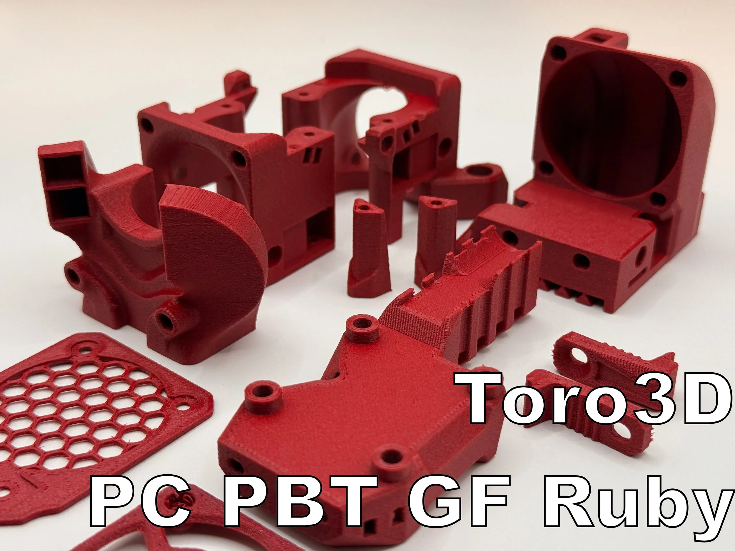 Verschiedene rote 3D-gedruckte Kunststoffteile auf weißem Hintergrund, mit Text 'Toro 3D PC PBT GF Ruby Red