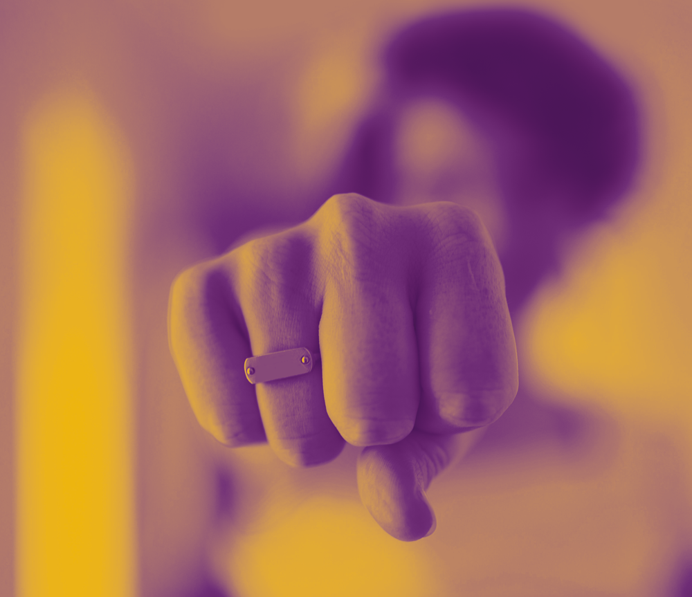 Person with a blurred face pointing at the camera, wearing a ring on their finger, with a purple and yellow color filter.