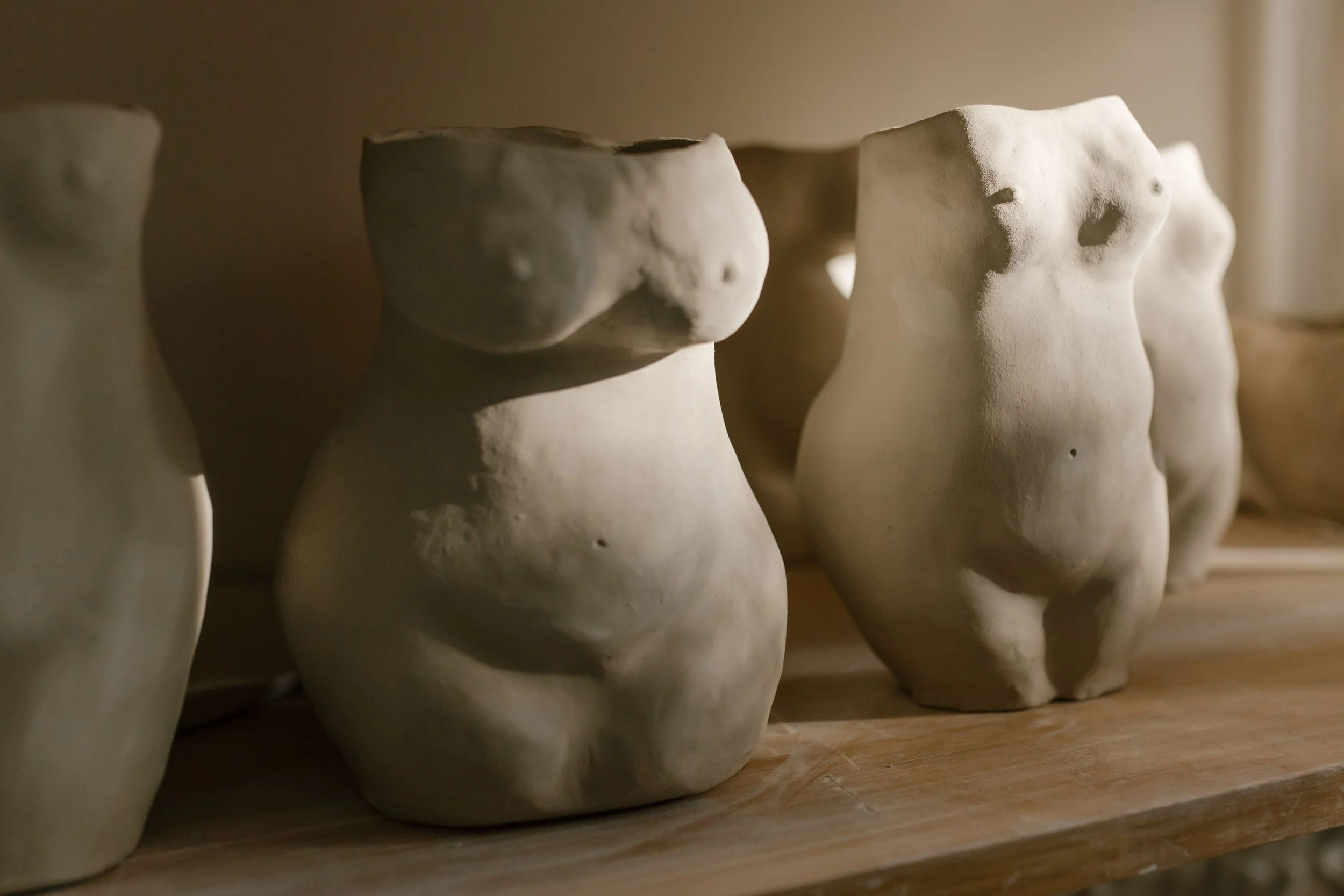 Close-up view of several abstract ceramic sculptures resembling human torsos, arranged on a wooden surface.