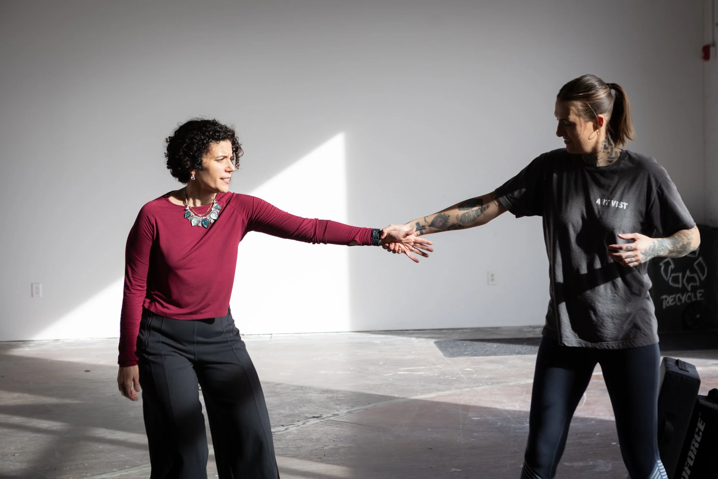 Two women practicing martial arts in a studio, with one woman holding the other's hand.