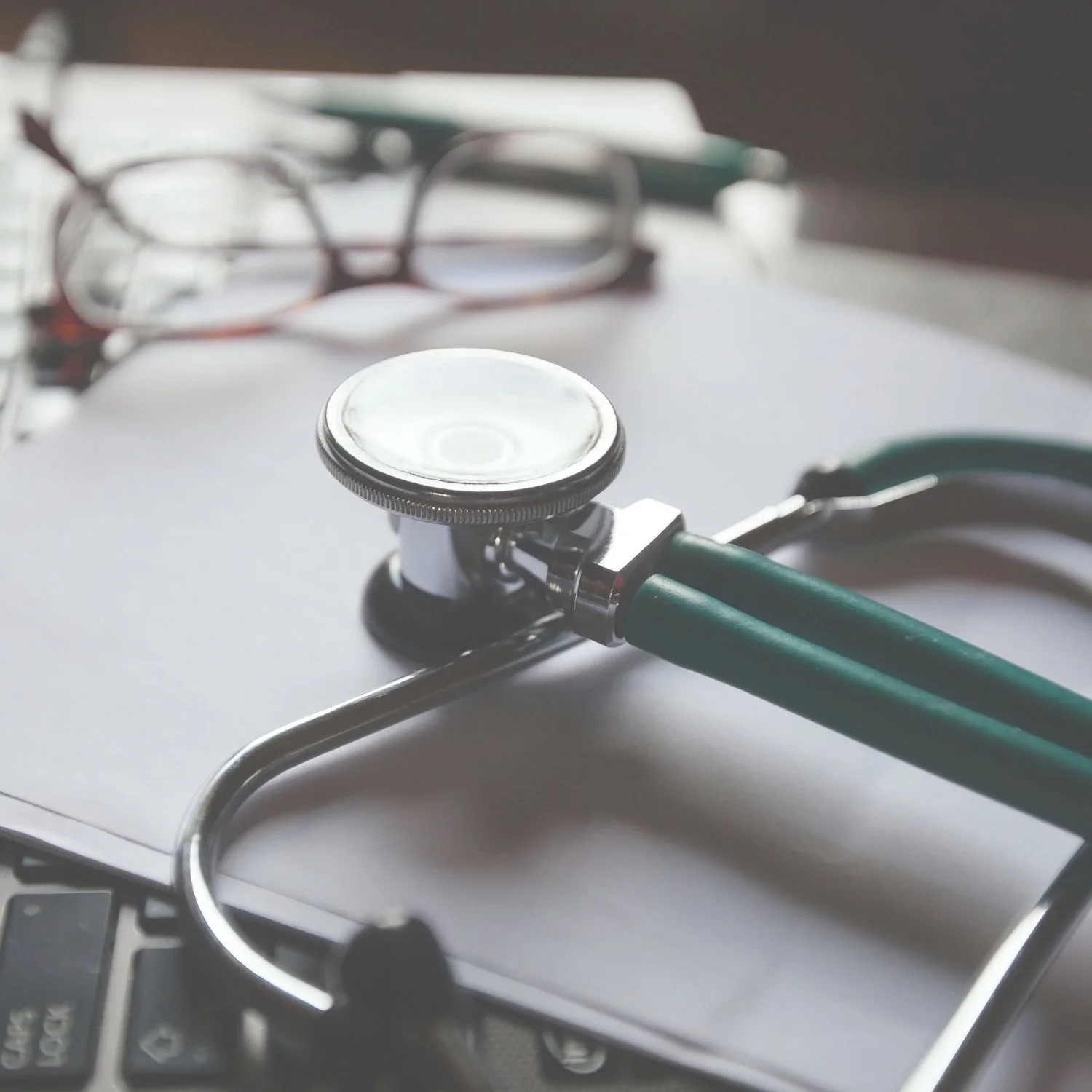 A stethoscope and eyeglasses resting on a laptop keyboard with papers in the background.