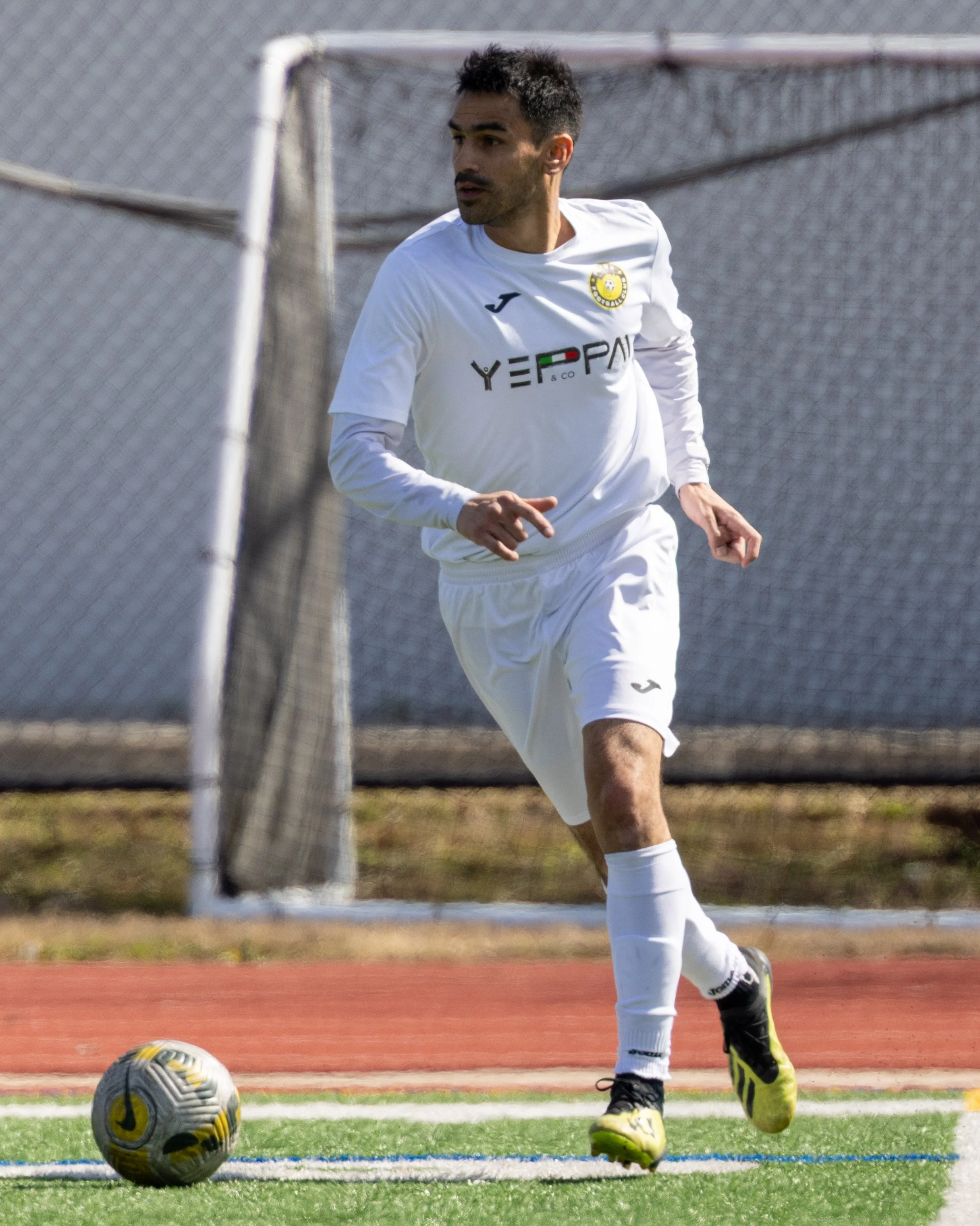 A soccer player in white uniform running on the field next to a soccer ball.