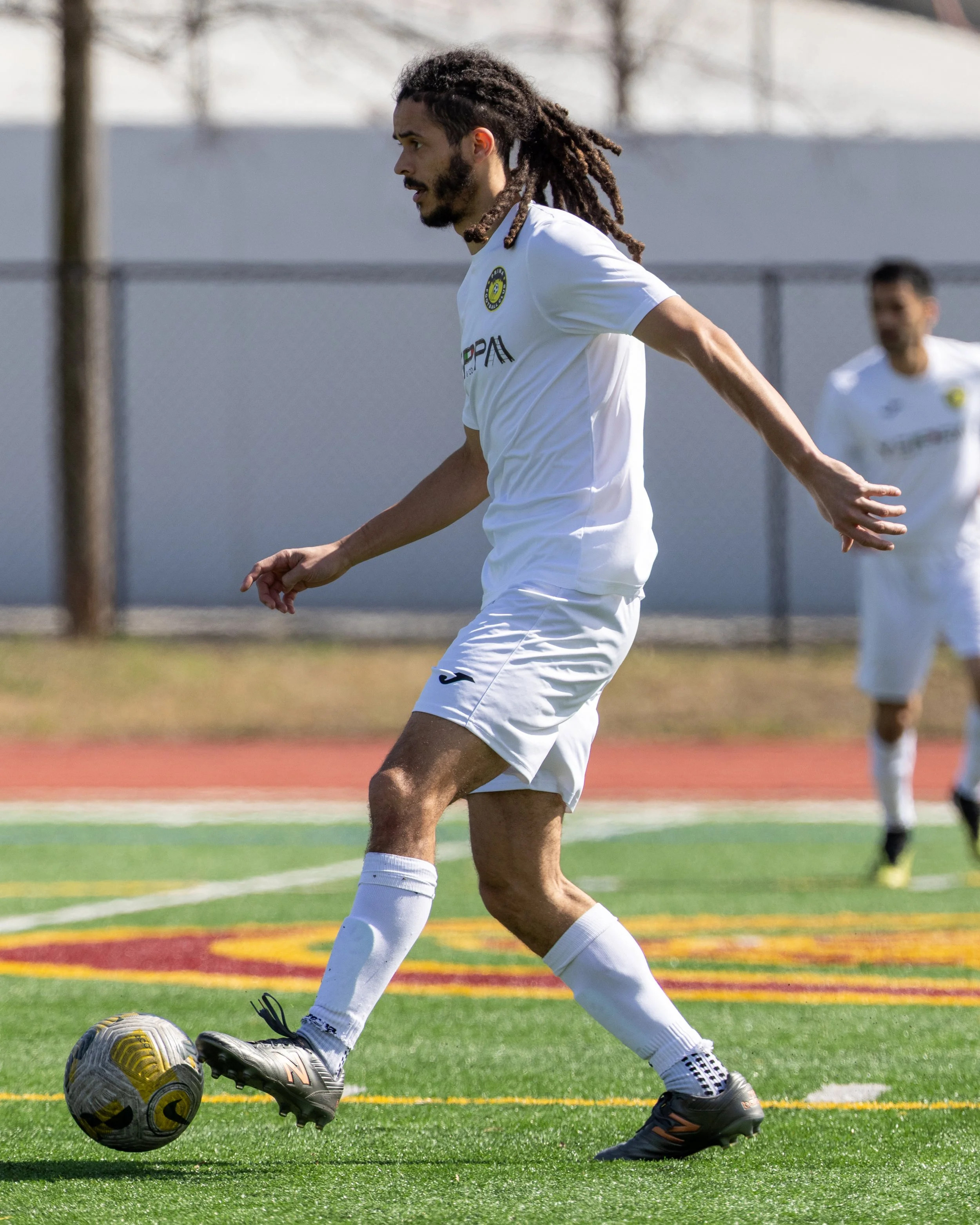 A soccer player in a white uniform with dreadlocks controlling a soccer ball on the field during a game.