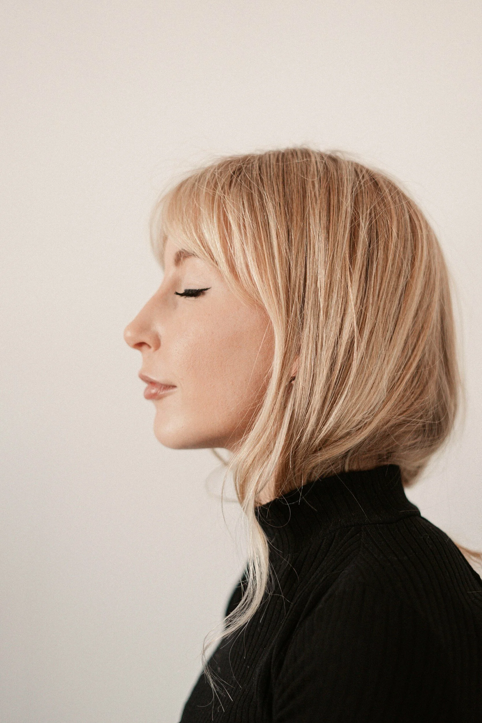 Profile of a woman with blonde hair in a black turtleneck, with eyes closed and a serene expression.