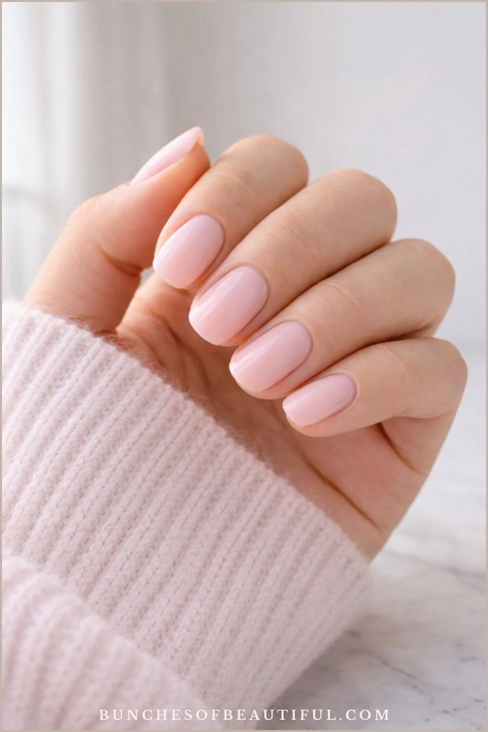 Simple spring nails with a glossy milky pink polish on short rounded nails photographed with a soft pink sweater sleeve.